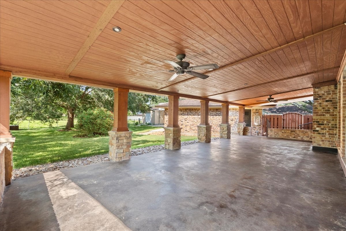 Expansive covered patio with ceiling fans and stone pillars, overlooking a lush green yard, perfect for outdoor entertaining.