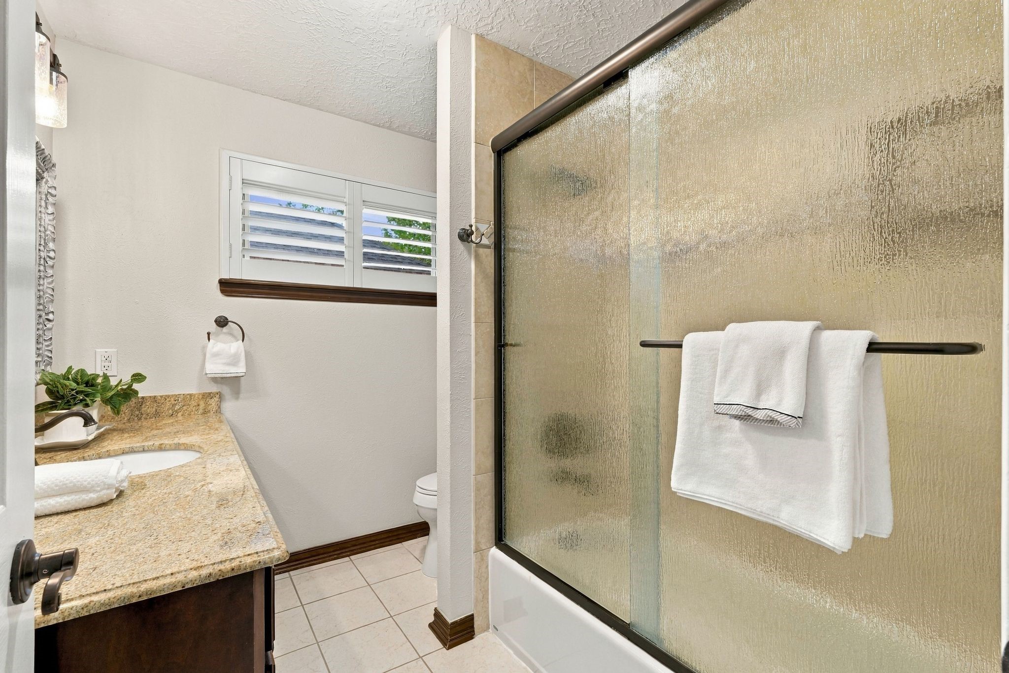 Bathroom featuring a glass-enclosed combination tub & shower, spacious vanity, and neutral finishes.