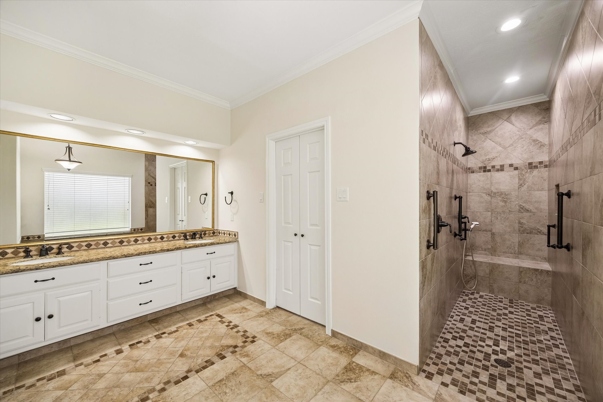 OVERSIZED PRIMARY BATH FEATURING AN EXPANSIVE DOUBLE VANITY, GRANITE COUNTERTOPS, AND A LARGE WALK-IN TILED SHOWER.