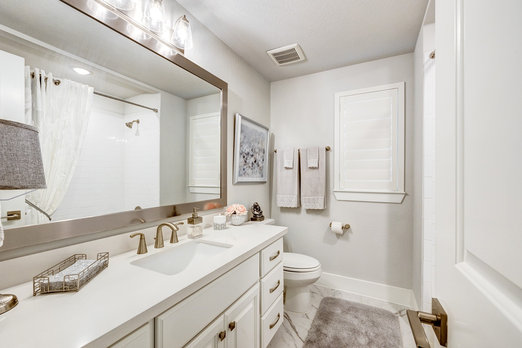 Upgraded bathroom featuring a custom-framed mirror and window shutters that provide both privacy and soft, natural light.