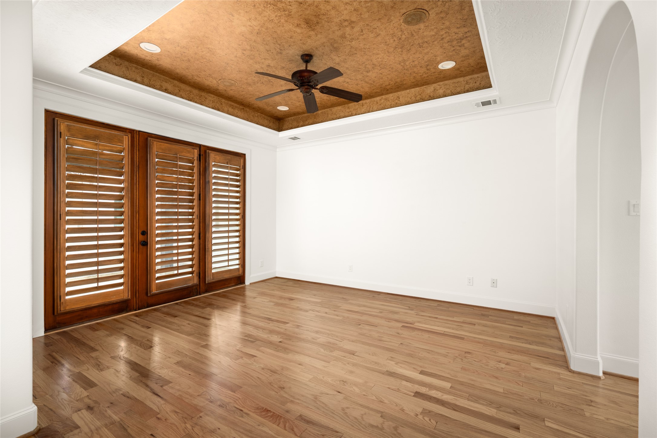 Third floor - Spacious primary suite featuring hardwood flooring, plantation shutters, and a distinctive tray ceiling with a ceiling fan.