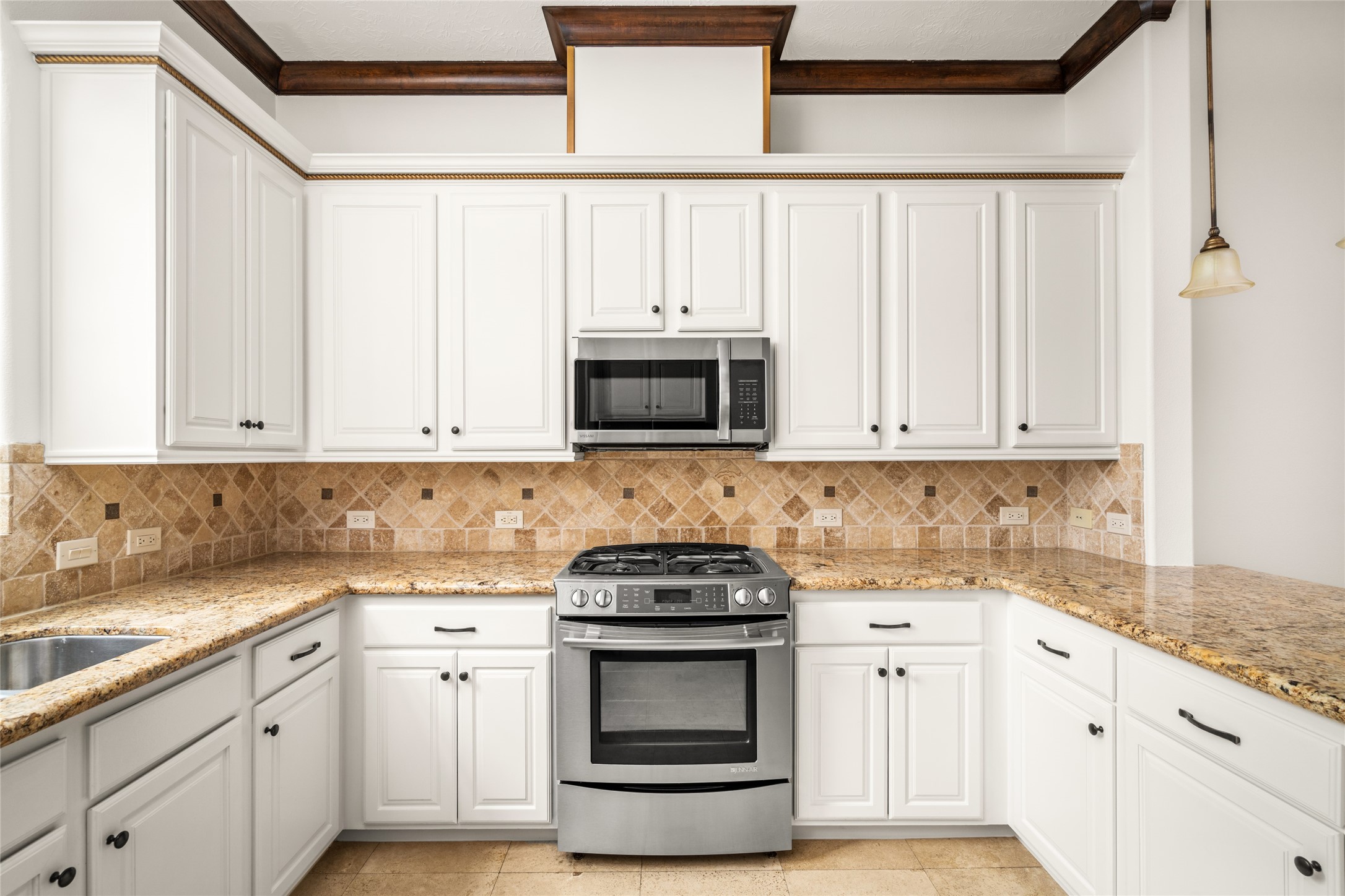Bright kitchen featuring white cabinetry, granite countertops, a decorative tile backsplash, stainless steel appliances, and elegant dark wood ceiling beams.