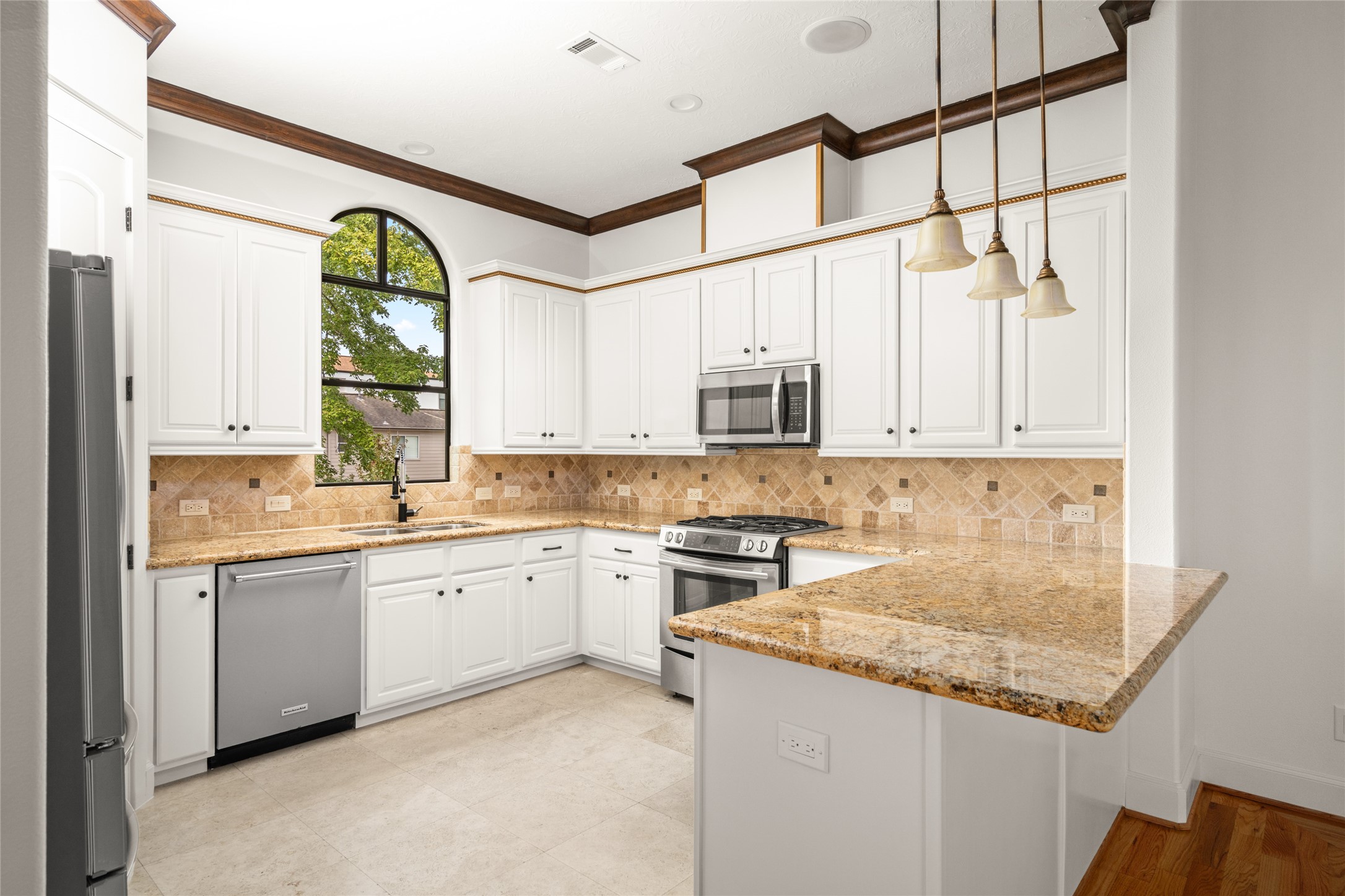 Second floor- Spacious kitchen with stainless steel appliances, travertine flooring, granite countertops, pendant lights, and plenty of storage.