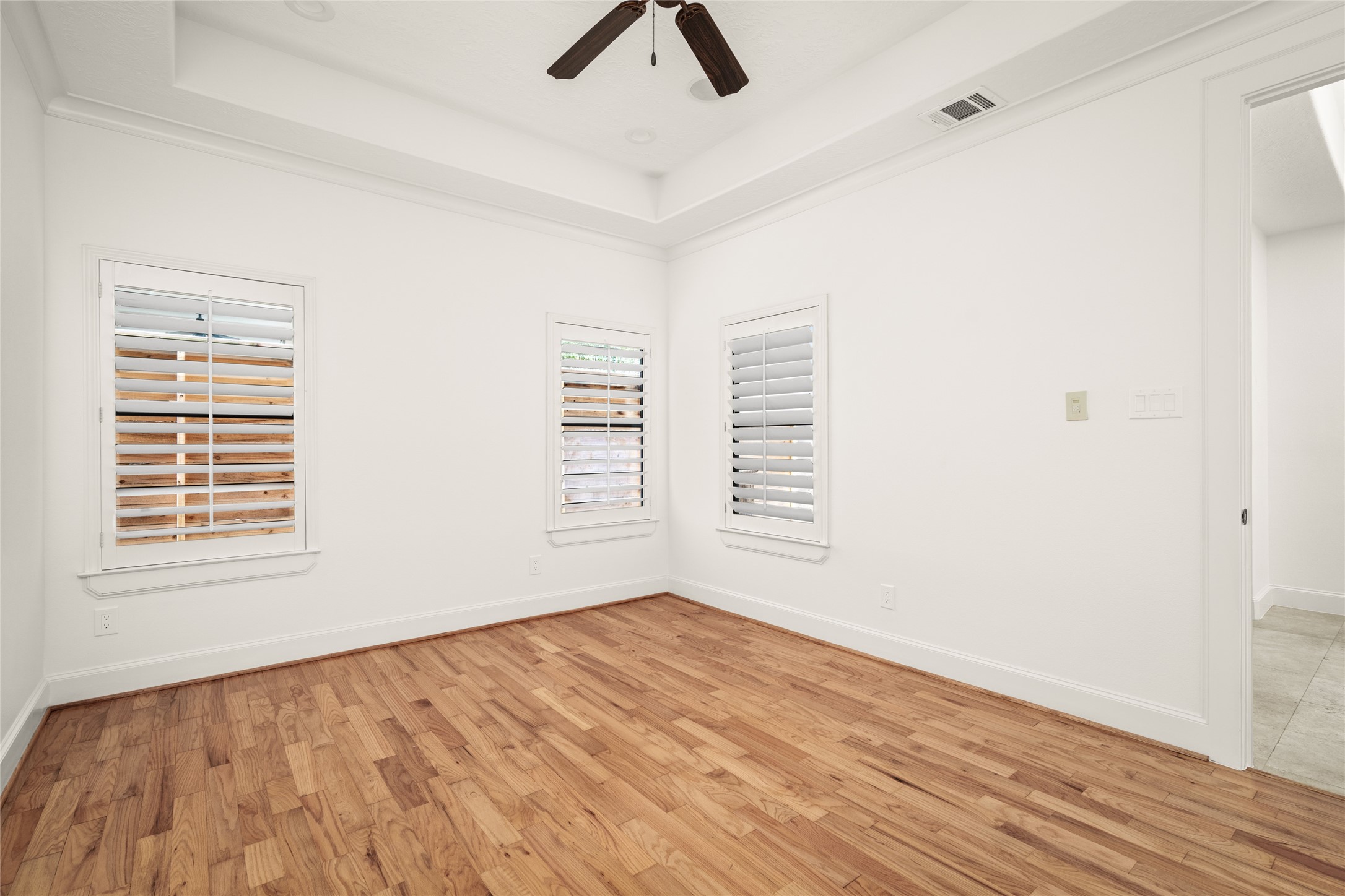 First floor bedroom with tray ceilings, recessed lighting, hardwood flooring, a full bathroom and a walk in closet.