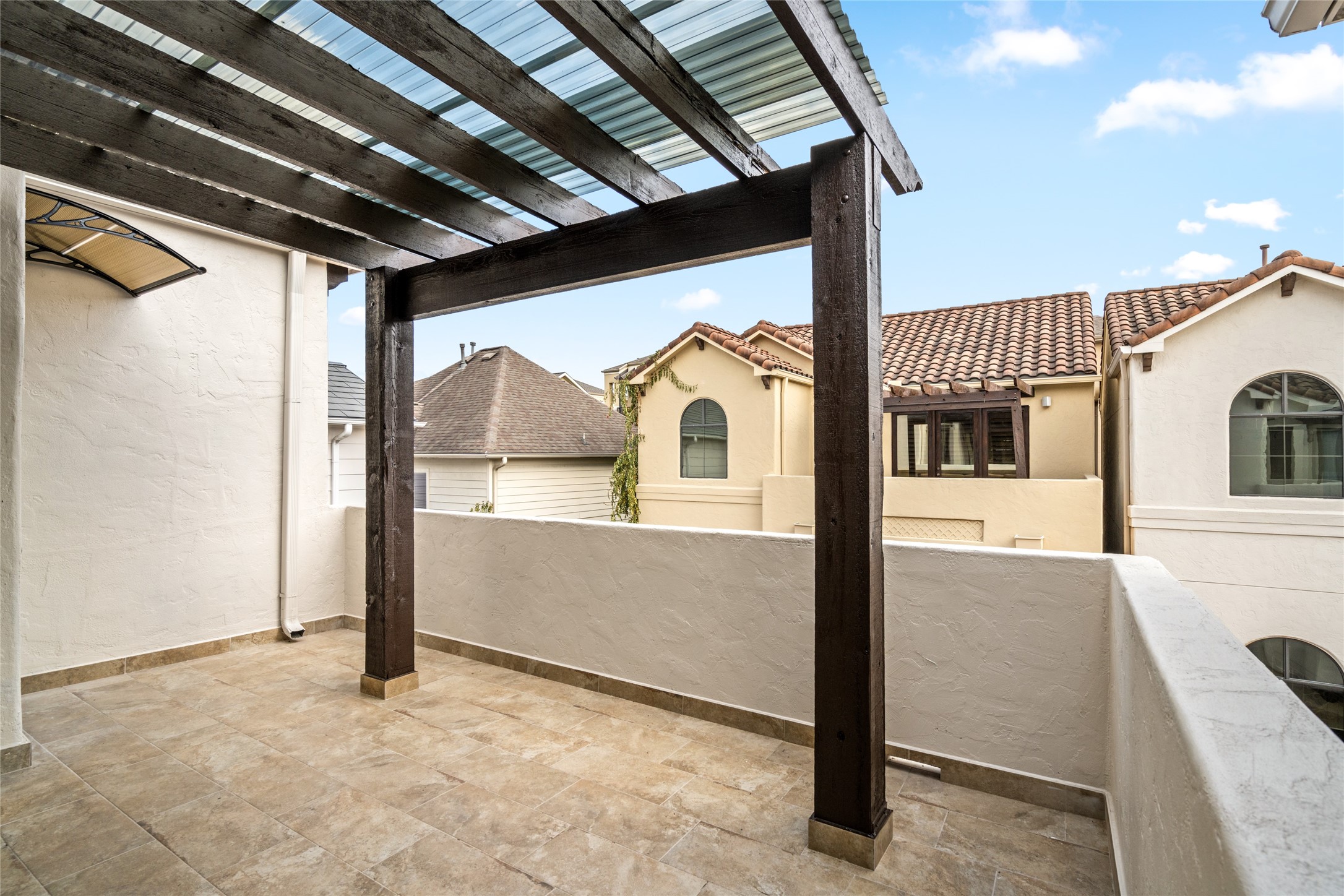 Enjoy outdoor relaxation on the private covered balcony, featuring warm tile flooring, rustic wood pergola beams, and neighborhood viewsan inviting space to unwind and enjoy the fresh air.