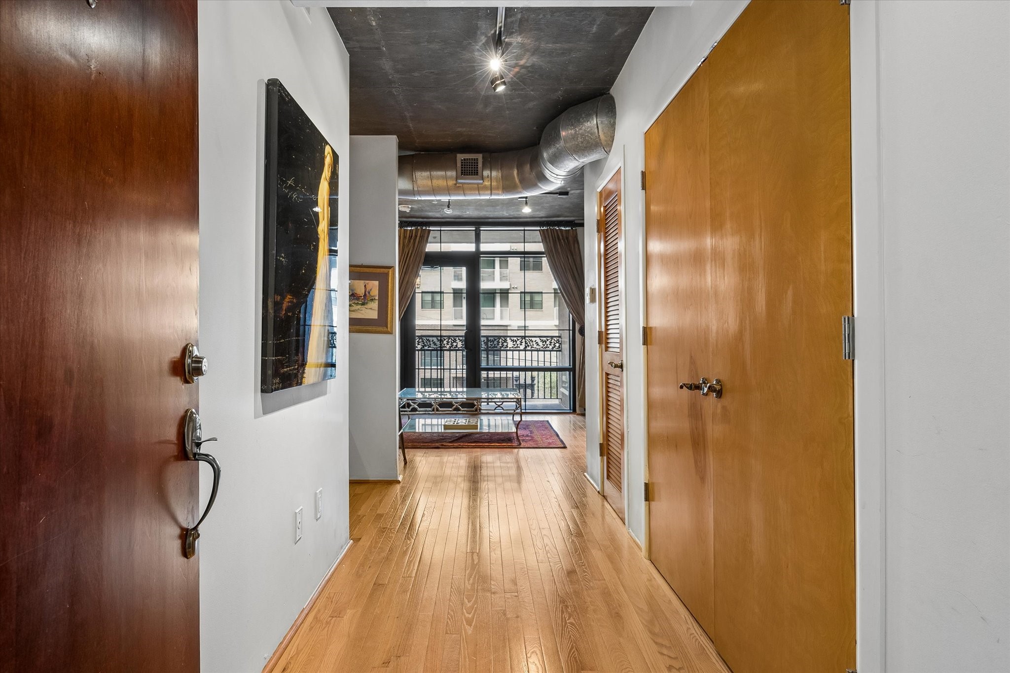 Step inside Residence 303, where warm hardwood flooring and exposed concrete ceilings introduce the home's distinctive industrial loft character. The entry hallway creates a natural transition into the open living spaces.