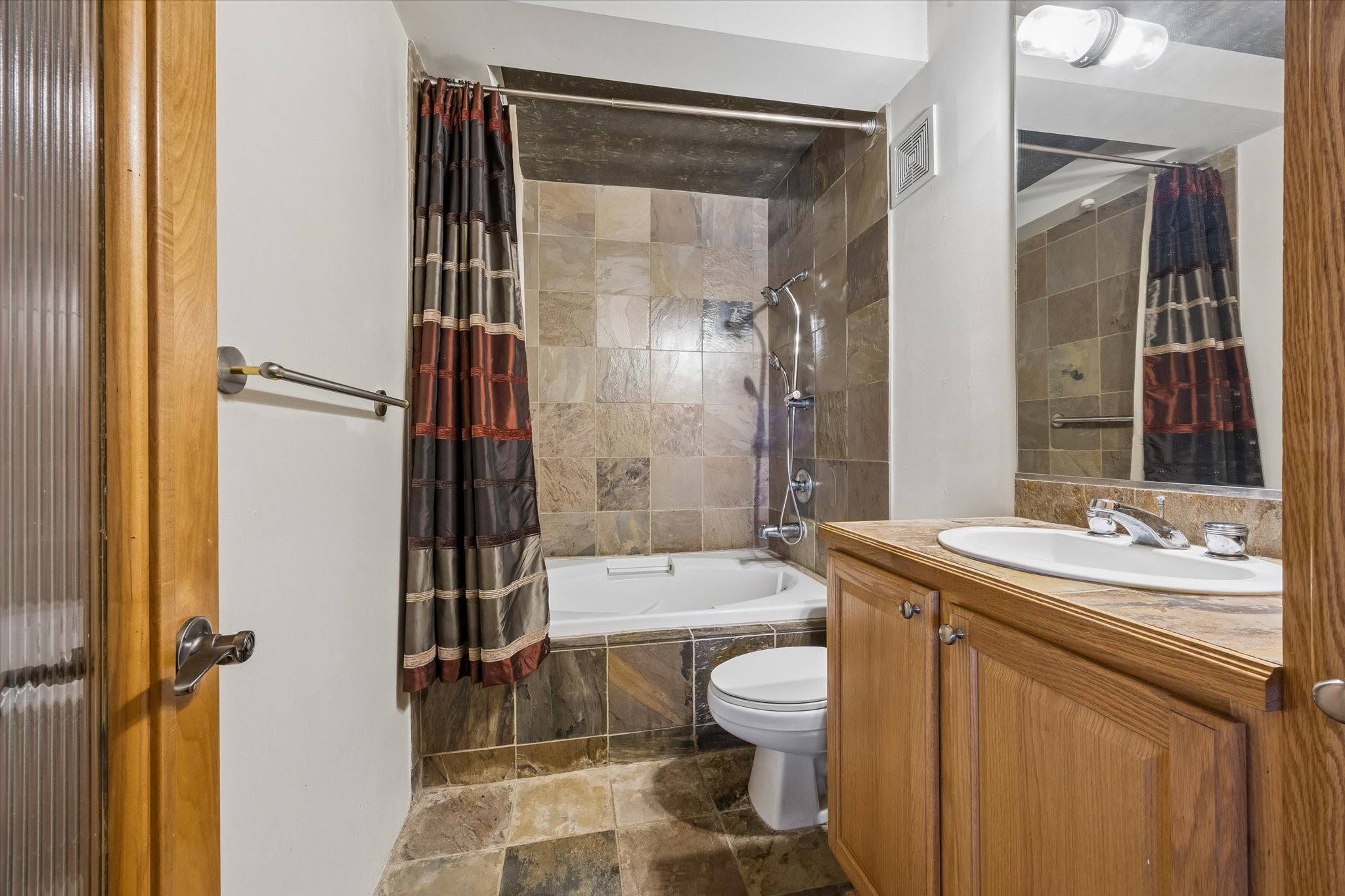 The bathroom features a spacious vanity with wood cabinetry, a large mirror, and a tub and shower combination. Neutral finishes and practical storage create a comfortable space for everyday routines.