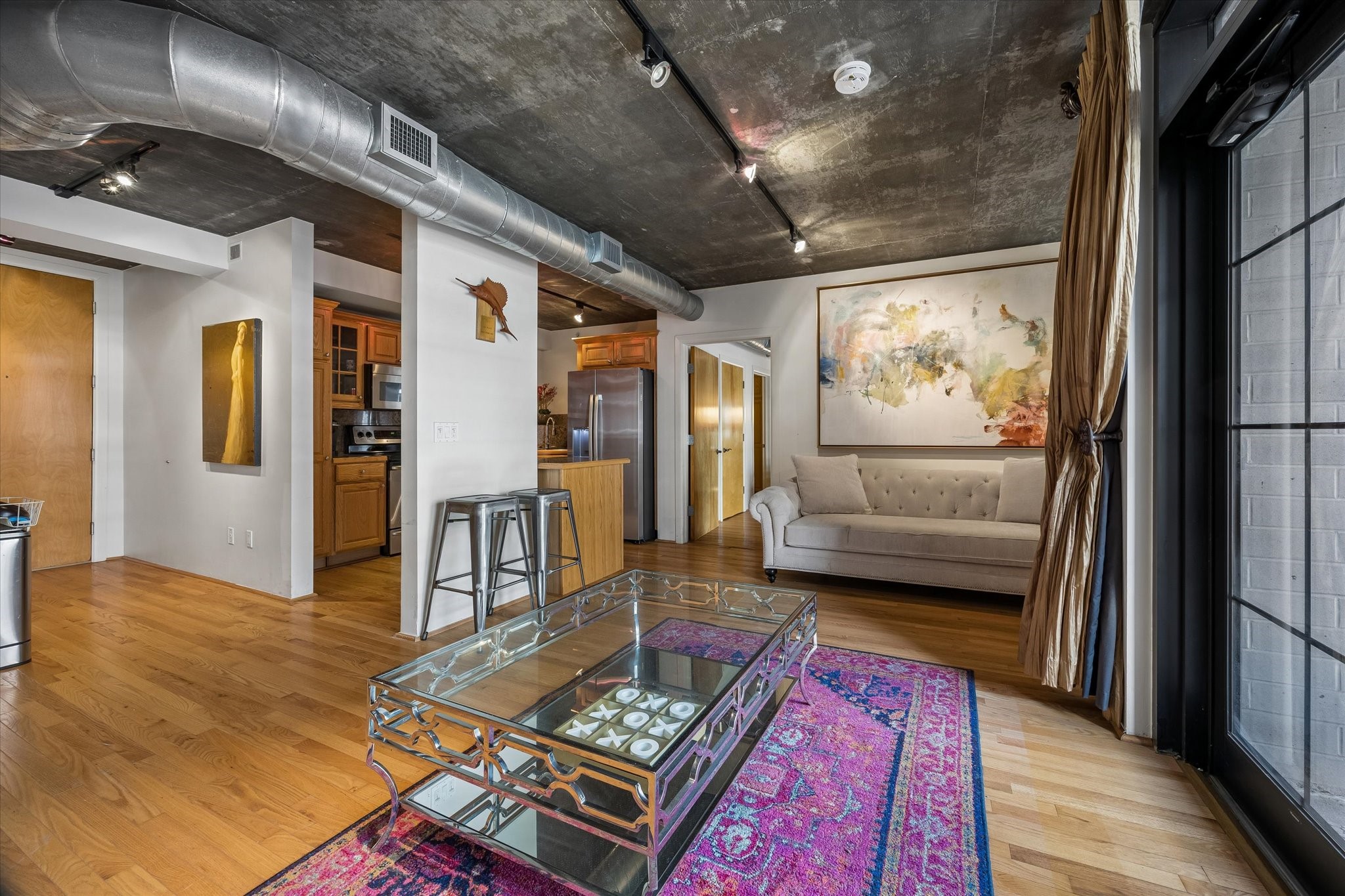 The living area combines exposed concrete ceilings, hardwood floors, and oversized windows for a distinctive loft-style atmosphere. An open layout provides flexibility for comfortable everyday living and entertaining.
