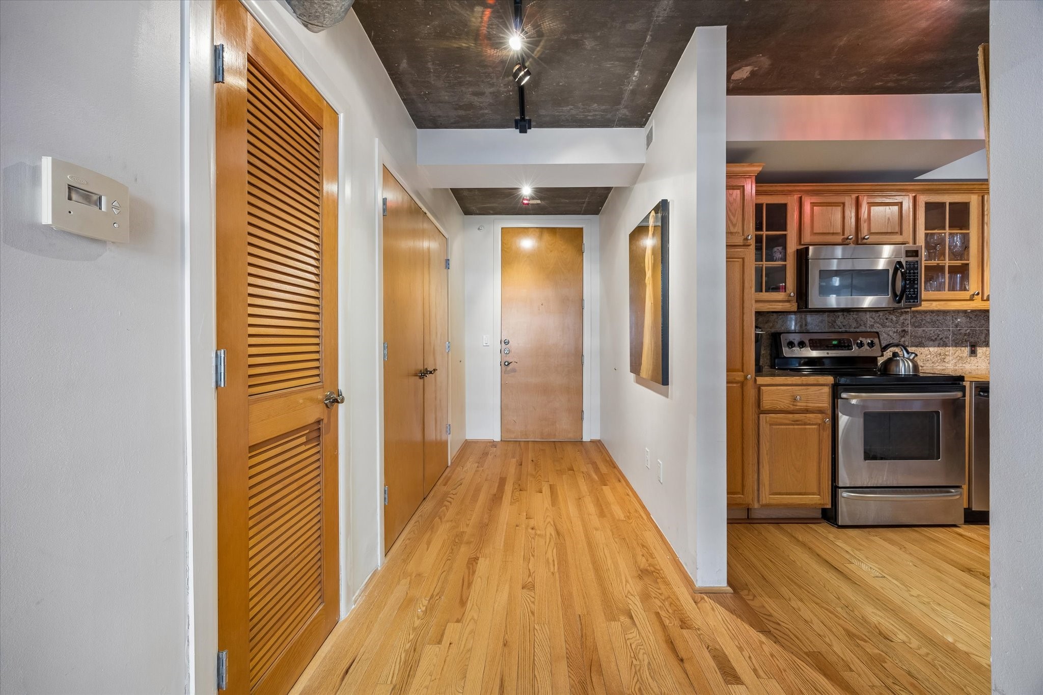 The thoughtfully designed floor plan connects the entryway to the kitchen and main living area. Natural wood finishes contrast beautifully with the exposed concrete ceilings, creating a warm, contemporary atmosphere.