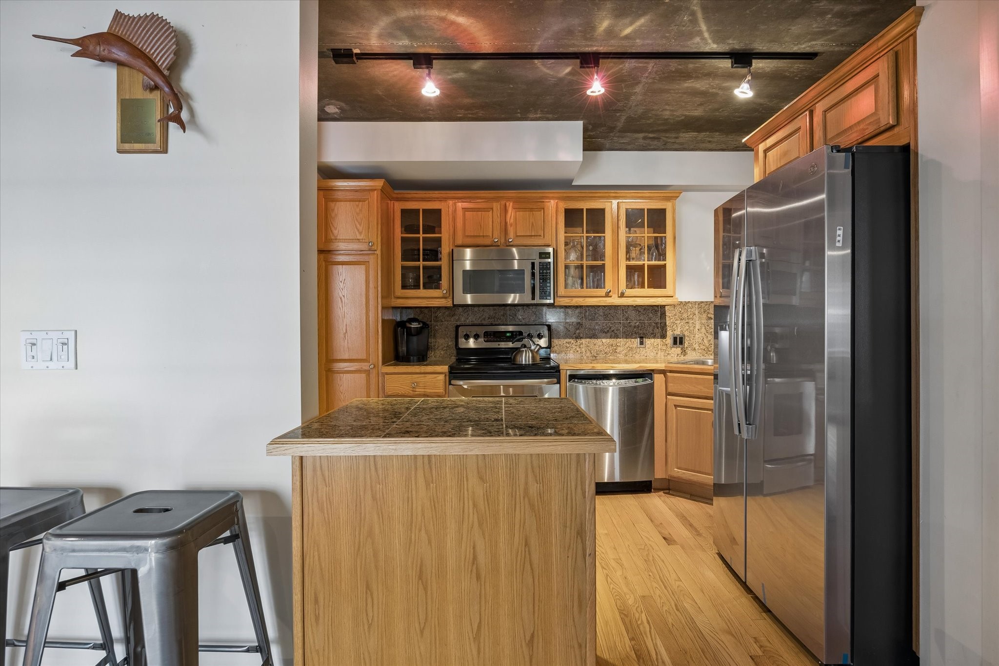The center island provides additional preparation space and a convenient gathering spot within the kitchen. Warm cabinetry, stainless steel appliances, and exposed concrete ceilings bring together practical design and industrial style.