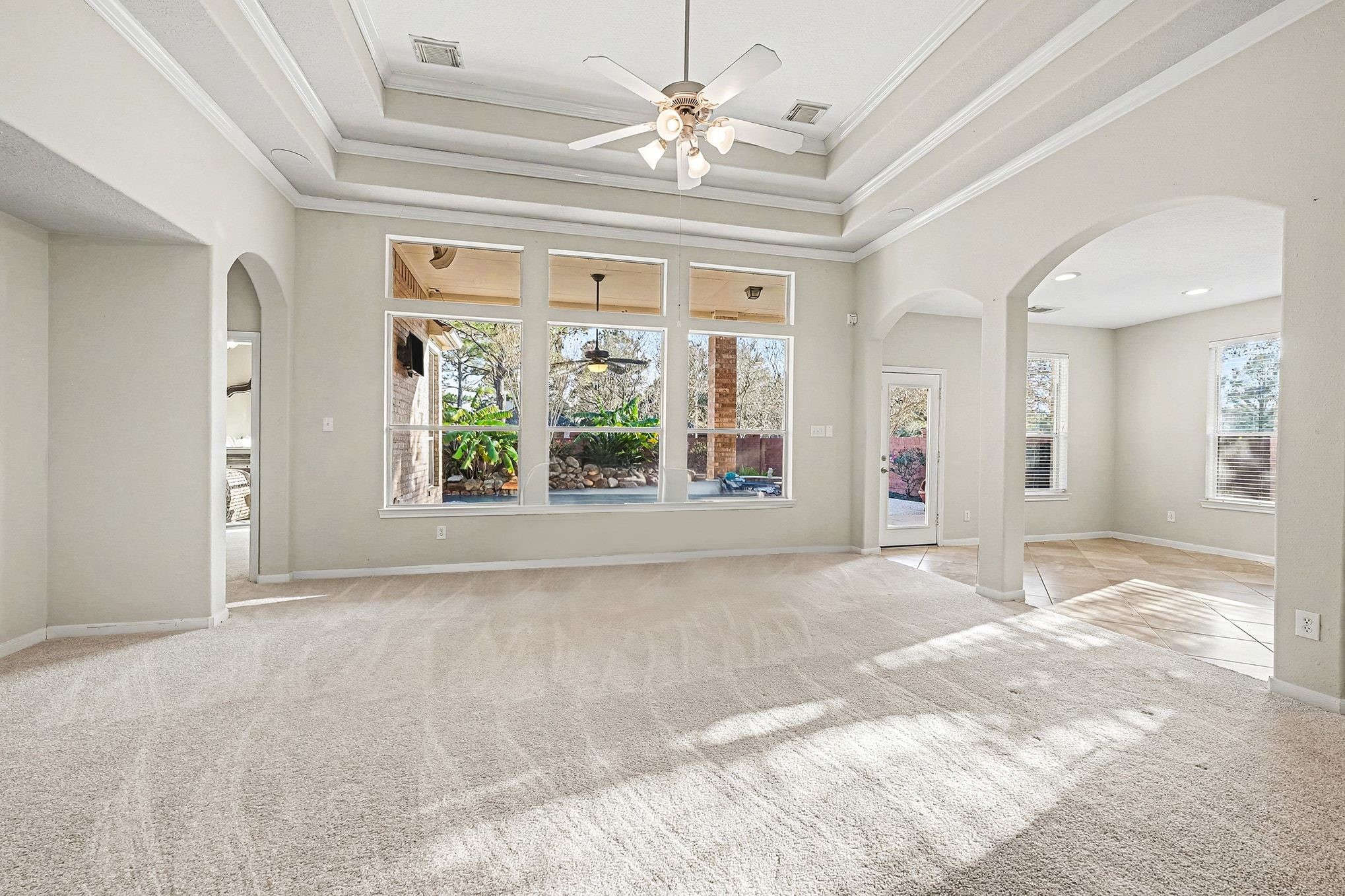 This shows another view of family room with no furniture featuring the wall of windows, arches, tray ceiling and  showing the backyard santuary.