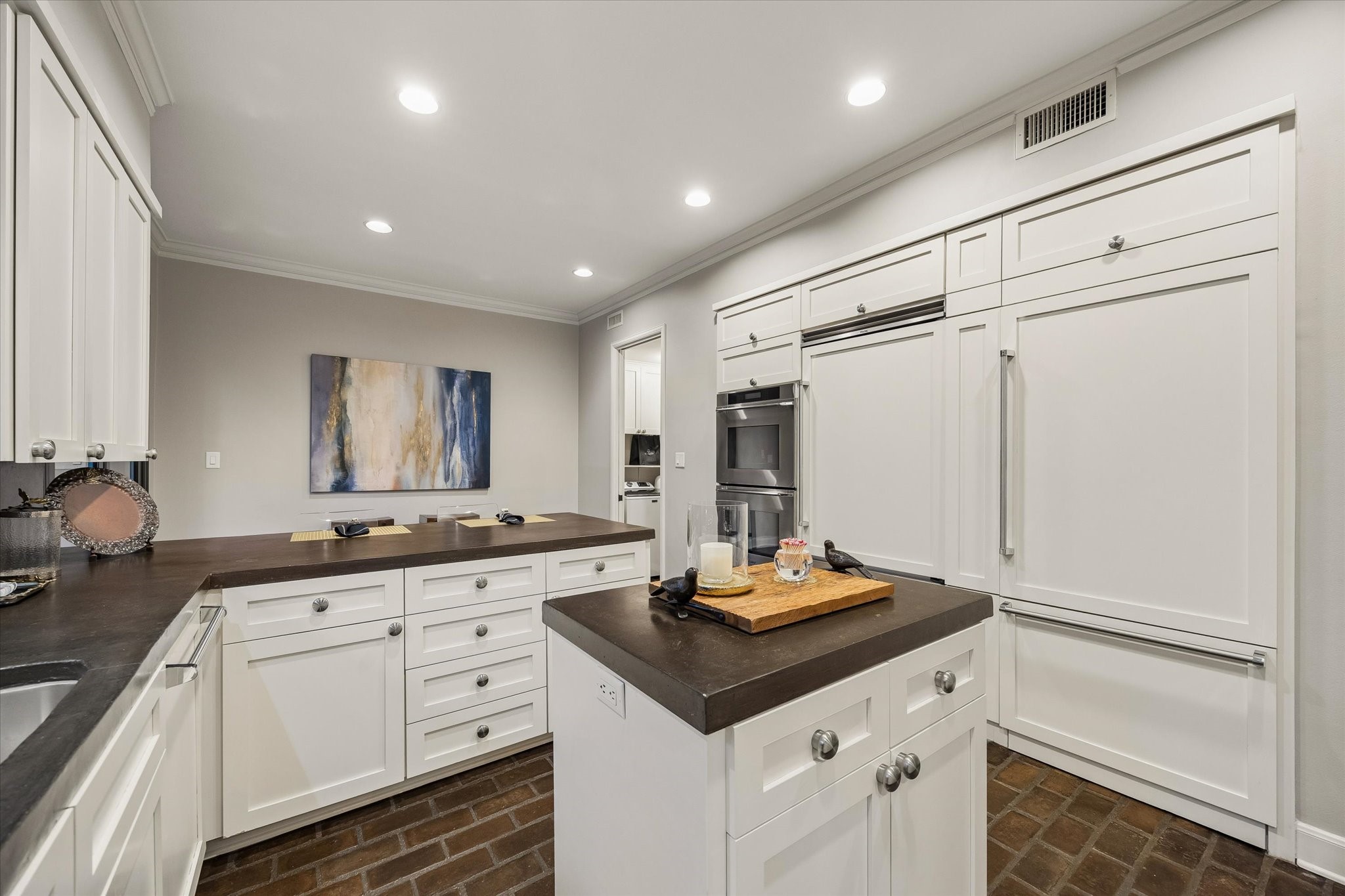 The Kitchen features a long 'U' shaped workspace plus an island.  Behind one of the doors on the right side of the frame is a SubZero refrigerator; behind the other is a walk-in Pantry.  Which one is which?!?