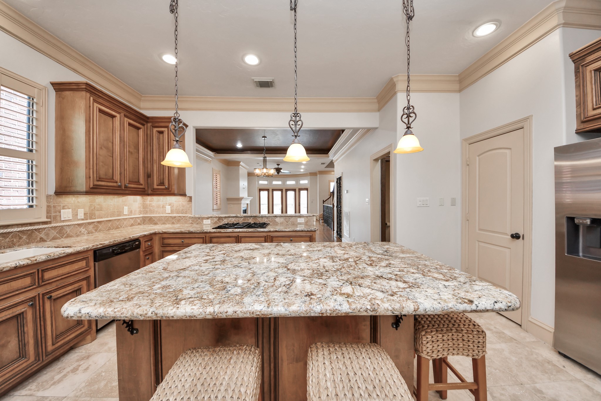 Spacious kitchen featuring elegant granite countertops, a central island with pendant lighting, and warm wood cabinetry, seamlessly flowing into a bright living area.