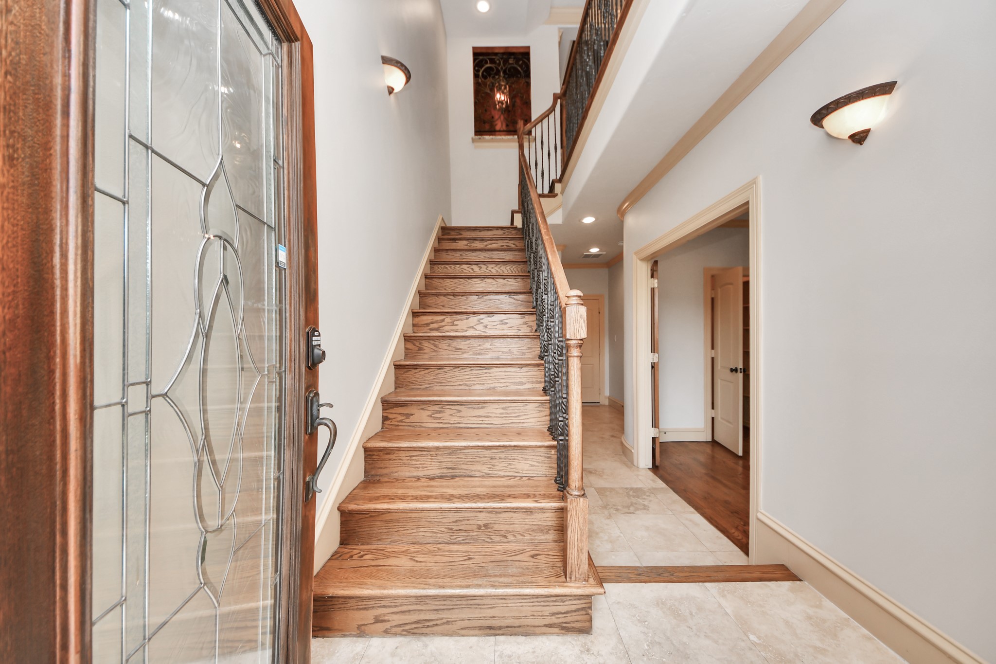 Elegant entryway featuring a striking wooden staircase with wrought iron balusters, and a beautifully detailed glass front door, leading into a spacious, light-filled hallway.