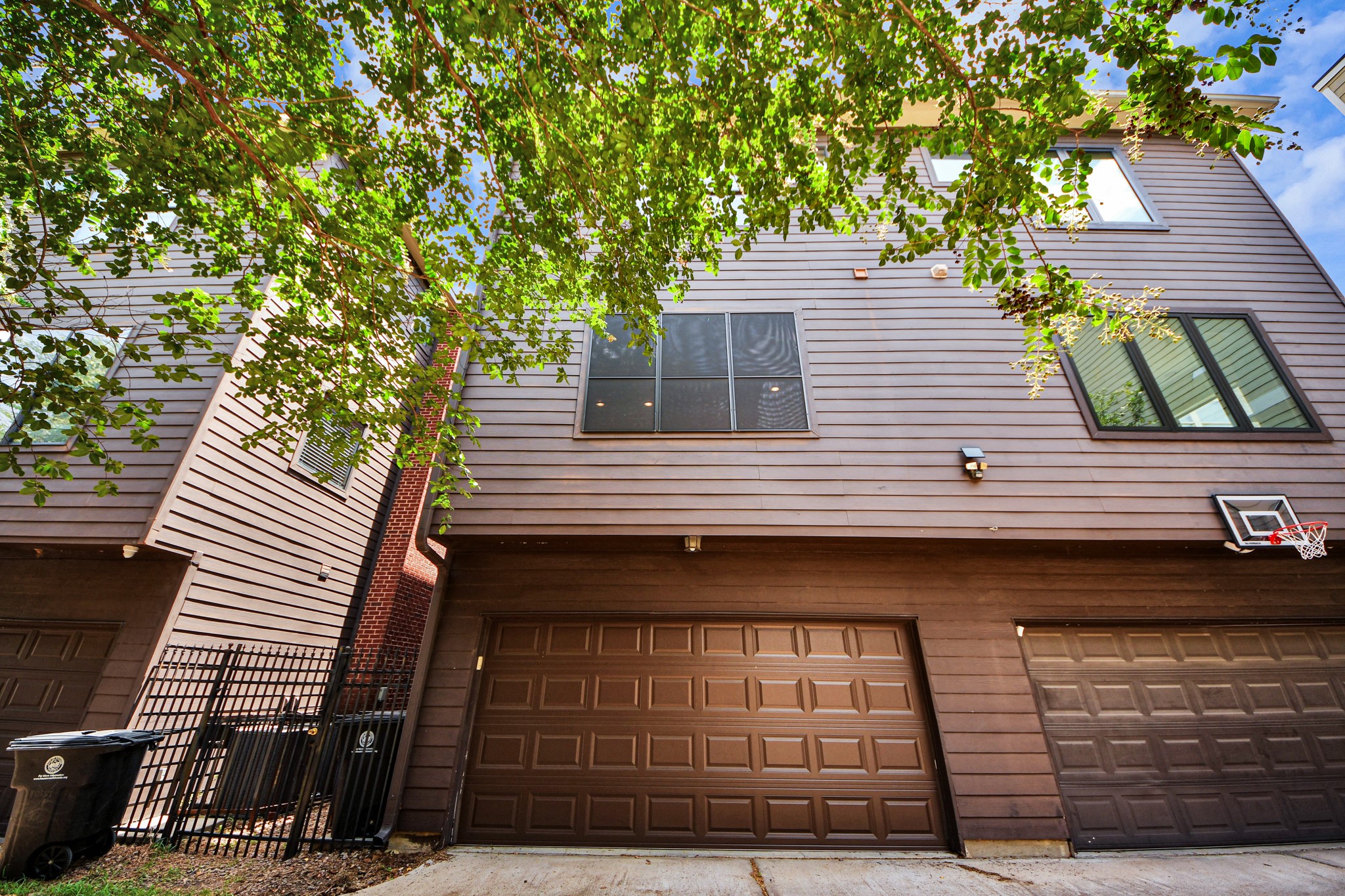 Modern townhouse with a brick and wood exterior featuring spacious two-car garage and large windows, surrounded by lush greenery.