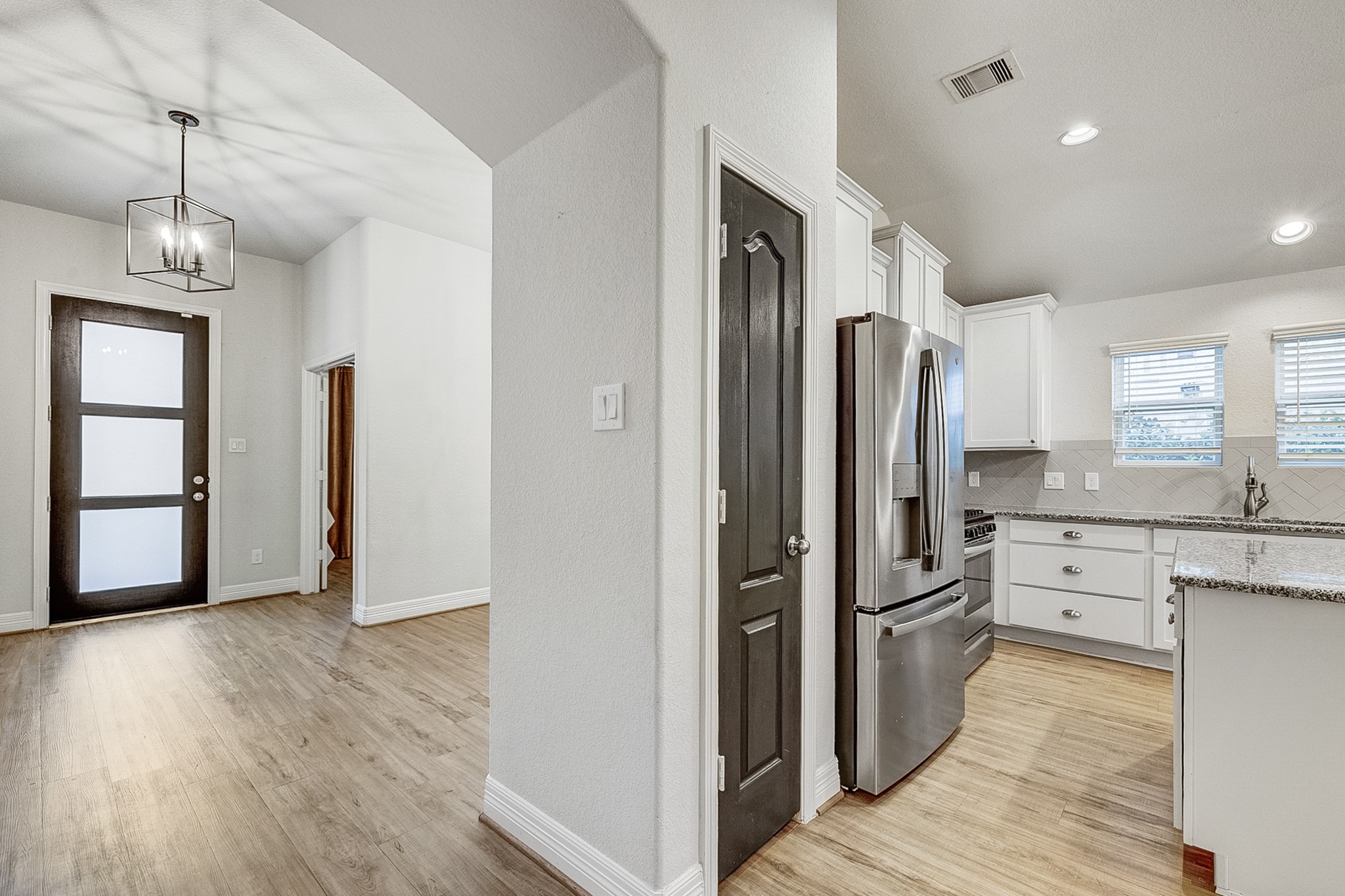 Bright, modern entryway with sleek hardwood flooring leads into a stylish kitchen featuring stainless steel appliances, granite countertops, and ample natural light from dual windows.