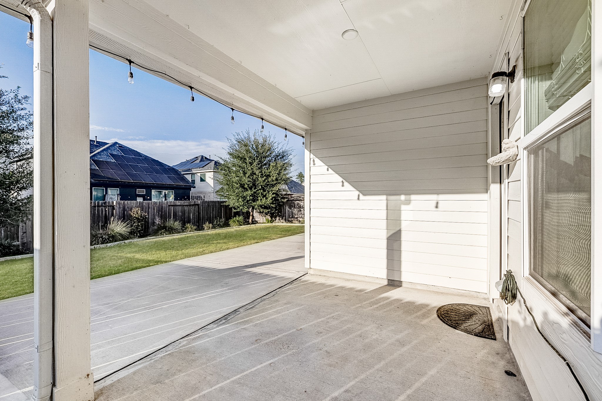 Charming covered patio with ample space, perfect for relaxing outdoors, overlooking a well-maintained backyard with lush grass and mature trees.