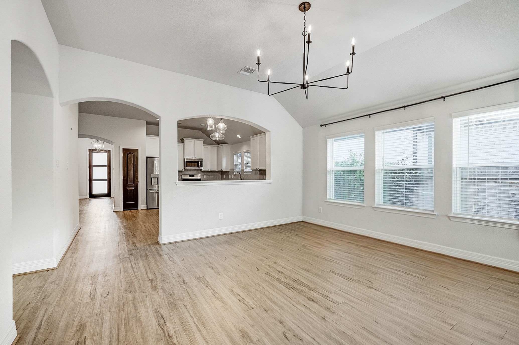 Bright and airy dining area with elegant hardwood flooring, a modern chandelier, and large windows offering ample natural light, seamlessly connected to the open kitchen and living space.