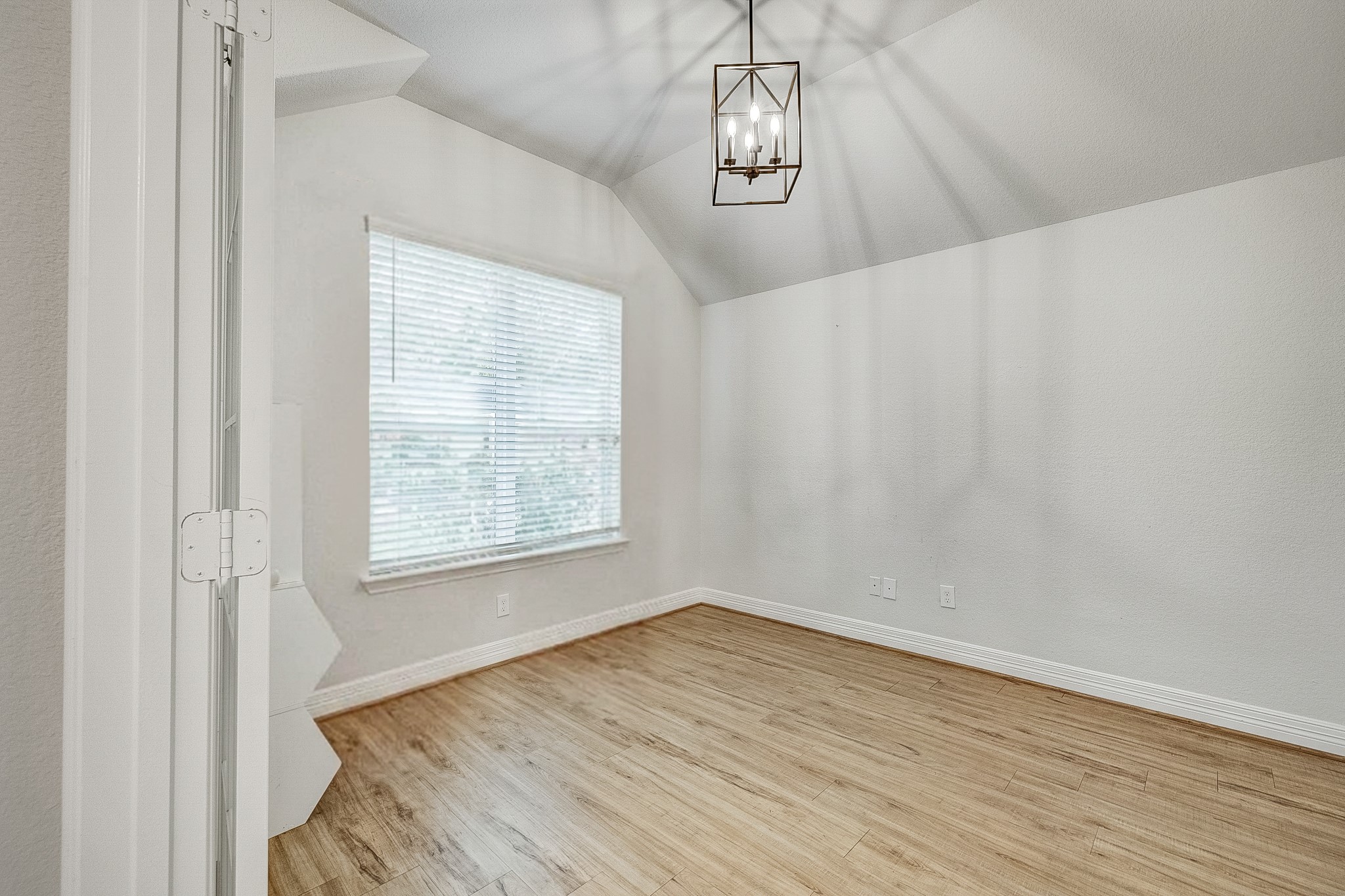Bright and inviting room featuring a modern light fixture, vaulted ceiling, and elegant wood flooring, perfect for an office or cozy retreat.