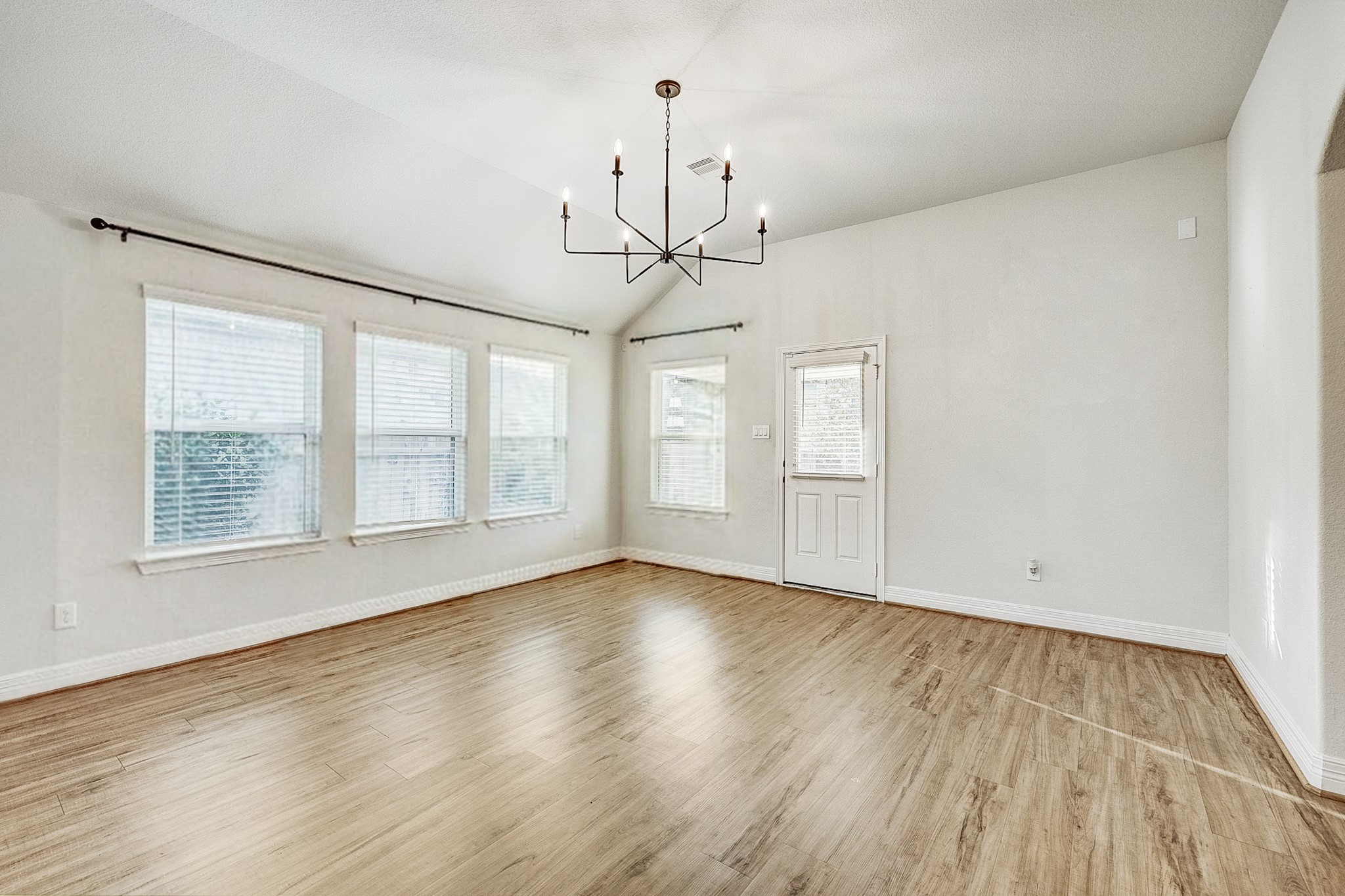 Bright and airy living space with large windows, elegant chandelier, and beautiful wood flooring.