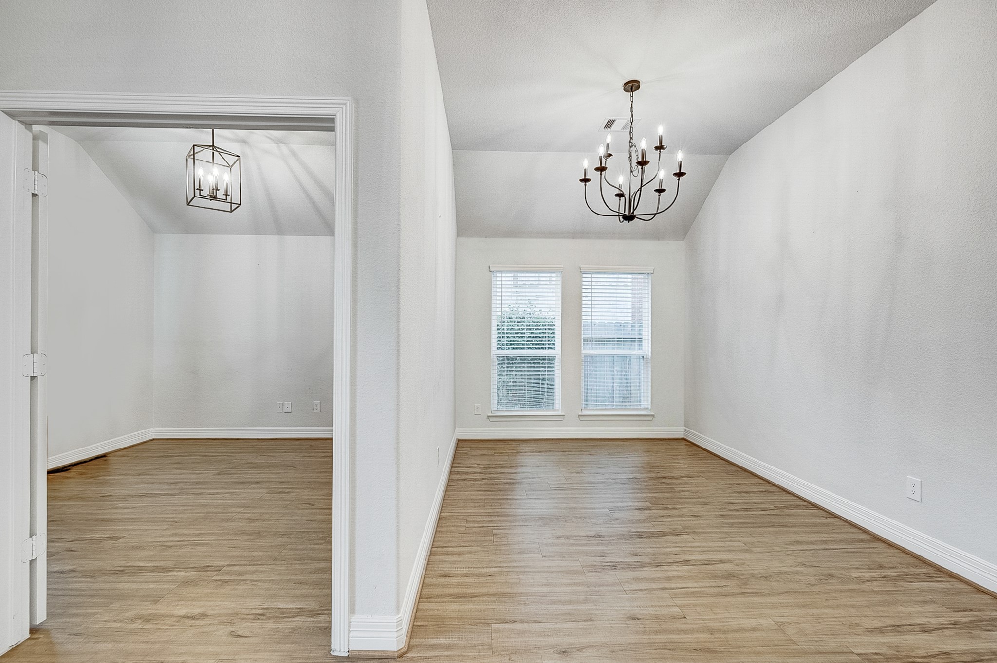 Bright and inviting dining area with wood flooring, elegant chandelier, and large windows for natural light. Adjacent space offers flexible use with modern lighting.