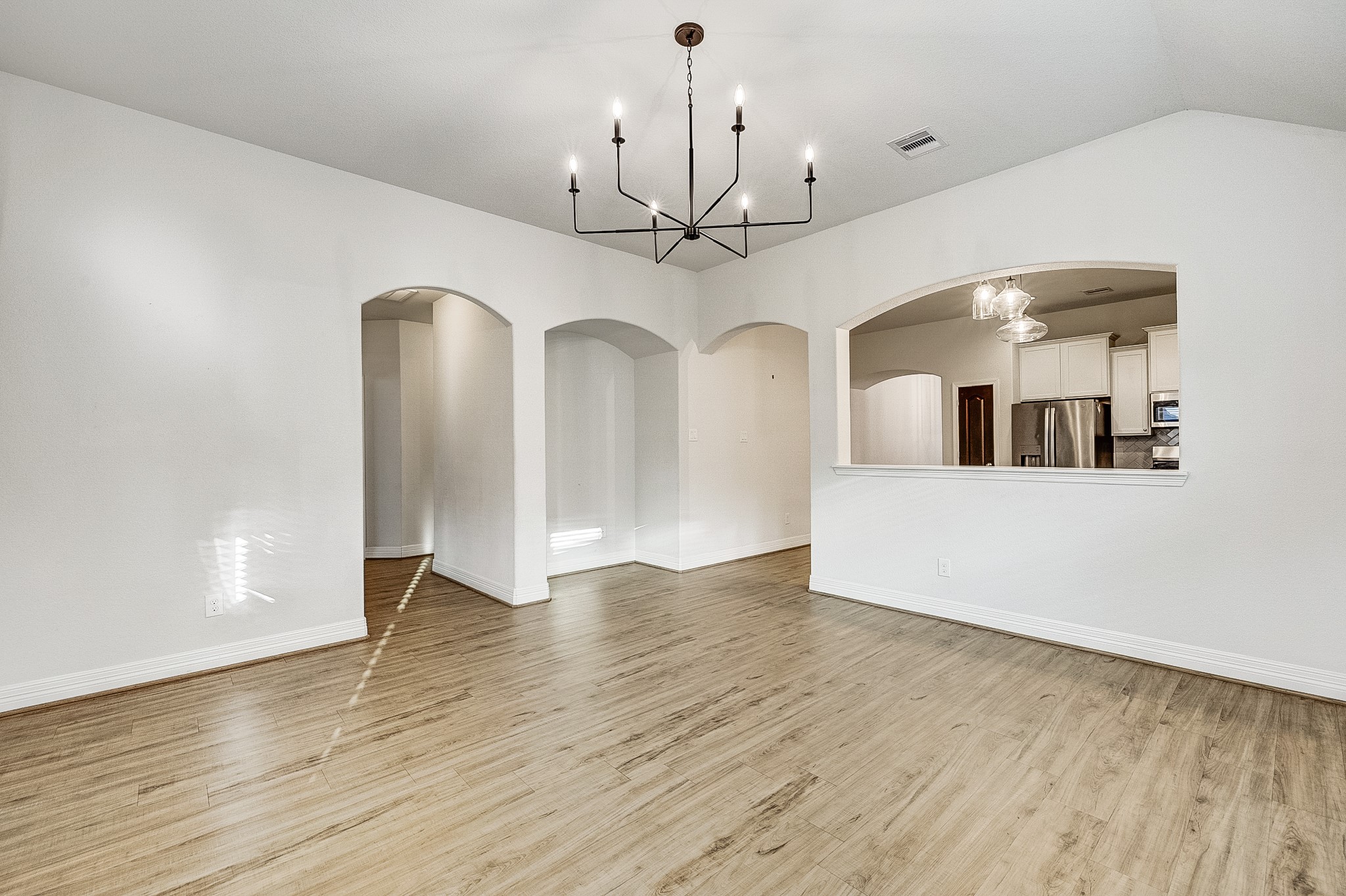 Bright and inviting open-concept space featuring elegant wood flooring, modern light fixtures, and charming arched entryways, seamlessly connecting to the kitchen area.