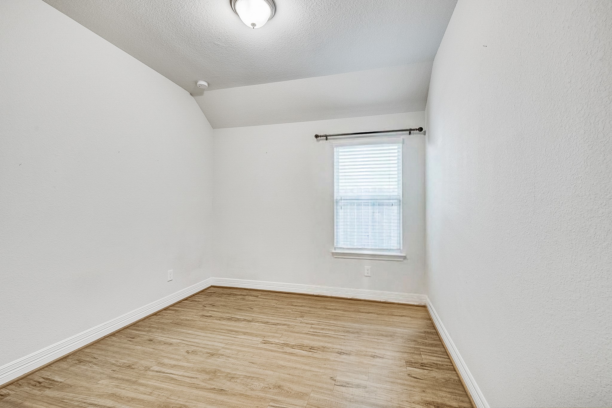 Bright and cozy room featuring hardwood floors, a single window for natural light, and clean white walls, perfect for a home office or guest room.