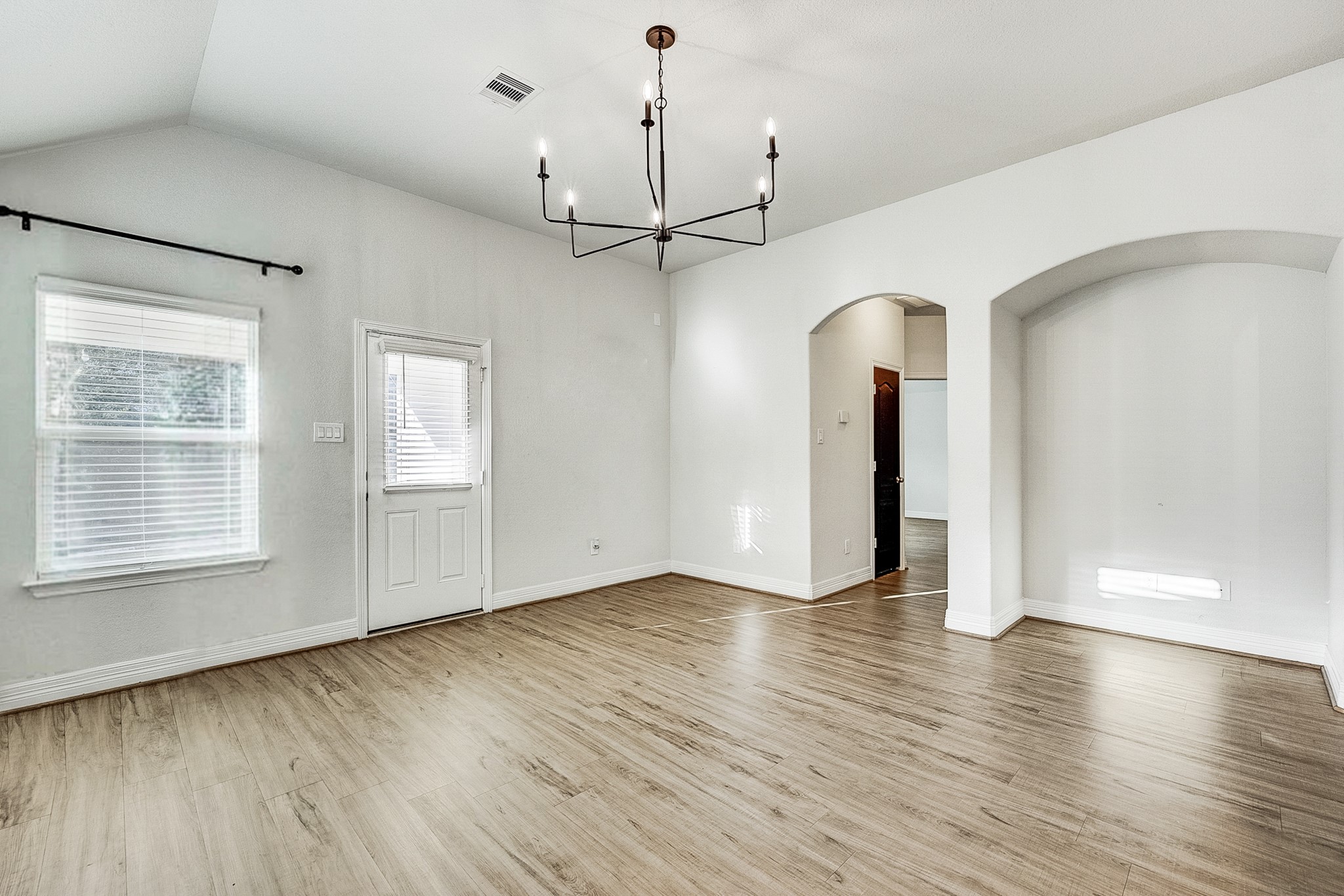 Bright and airy living space with high ceilings, elegant light fixture, and beautiful wood flooring, offering a welcoming and open atmosphere.