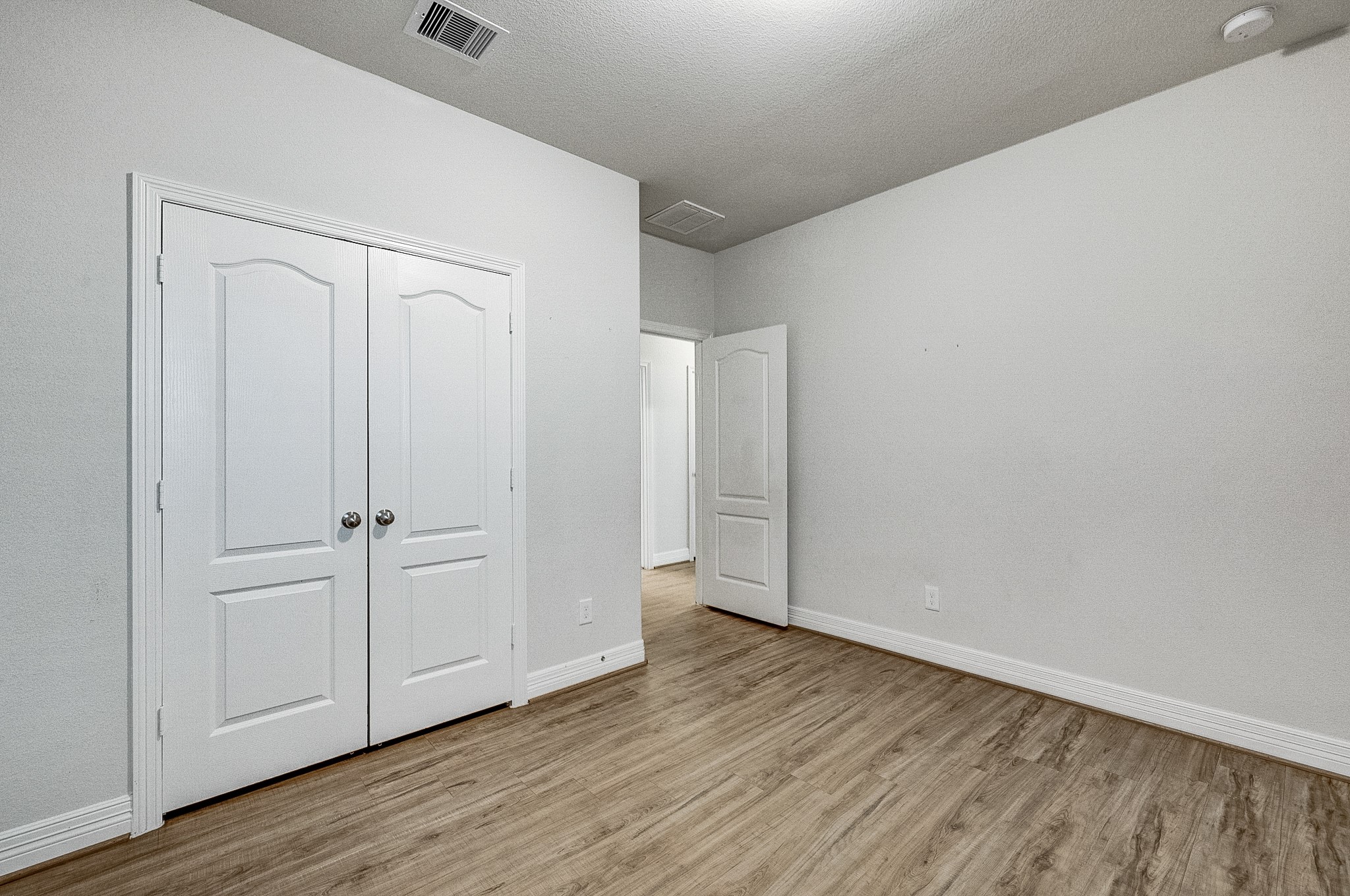 Spacious room with elegant wood flooring and a double-door closet, offering ample storage and a fresh, modern feel.