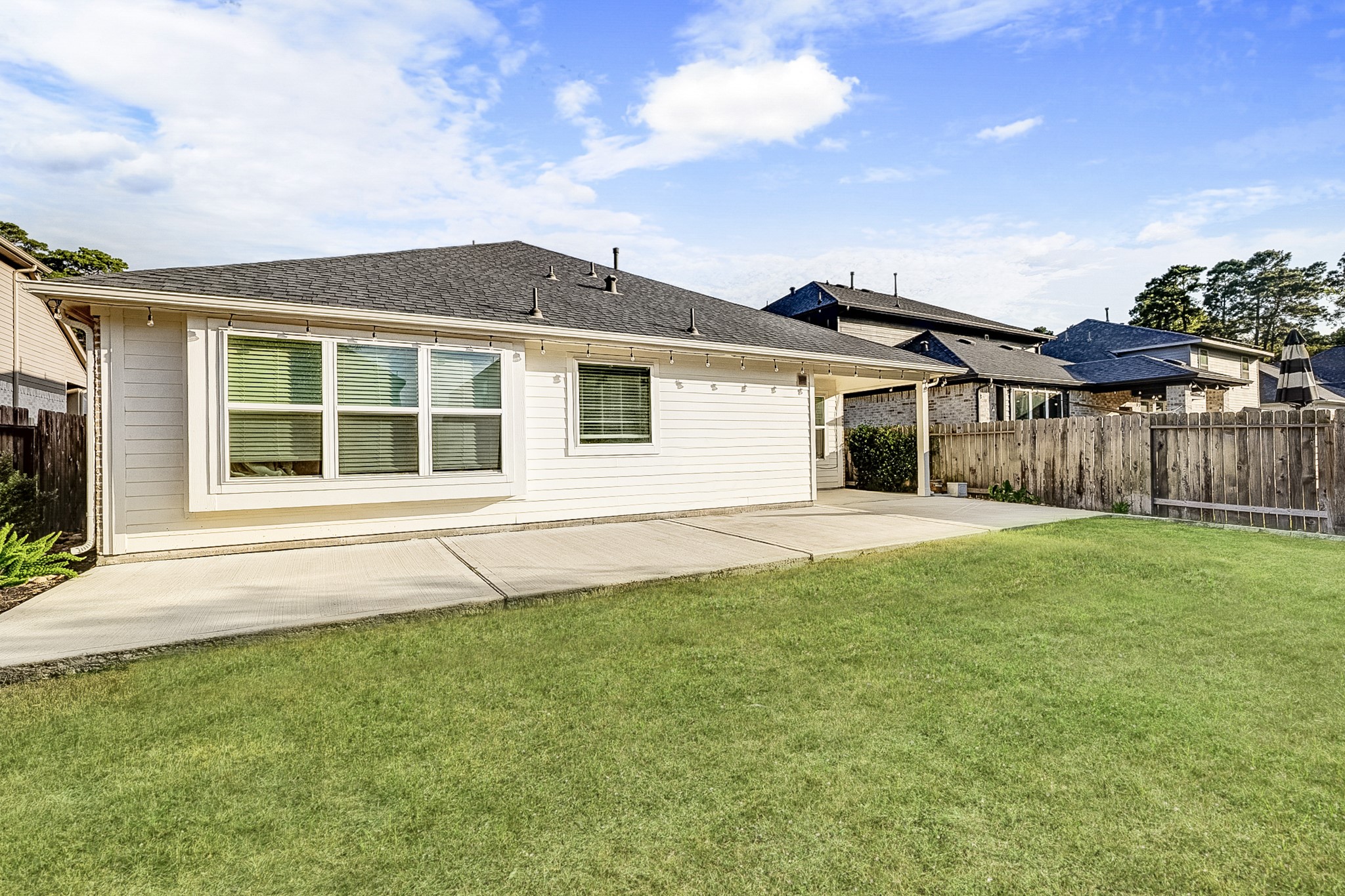 Charming backyard with a spacious patio, perfect for outdoor entertaining, bordered by a wooden fence for privacy and surrounded by lush greenery.