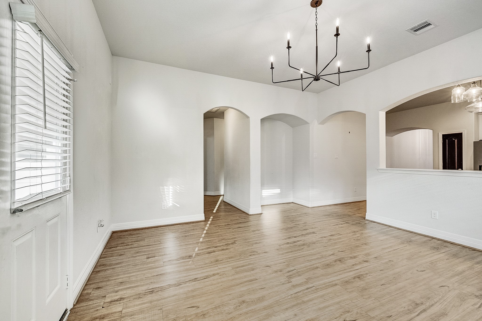 Elegant dining area with modern chandelier, hardwood floors, and arched doorways offering a spacious and inviting atmosphere.