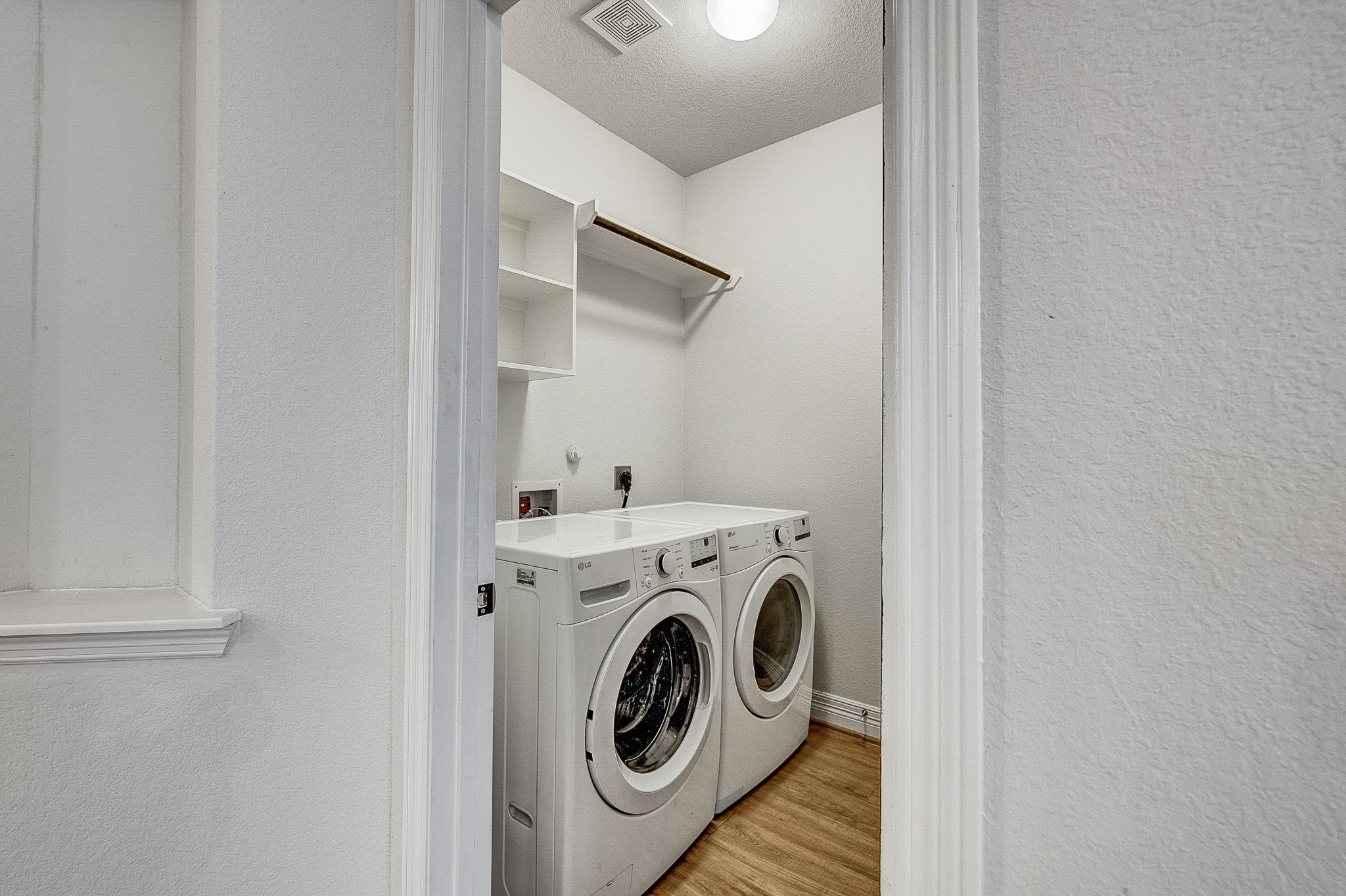 Efficient laundry room with modern washer and dryer, open shelving, and a hanging rod for convenience.
