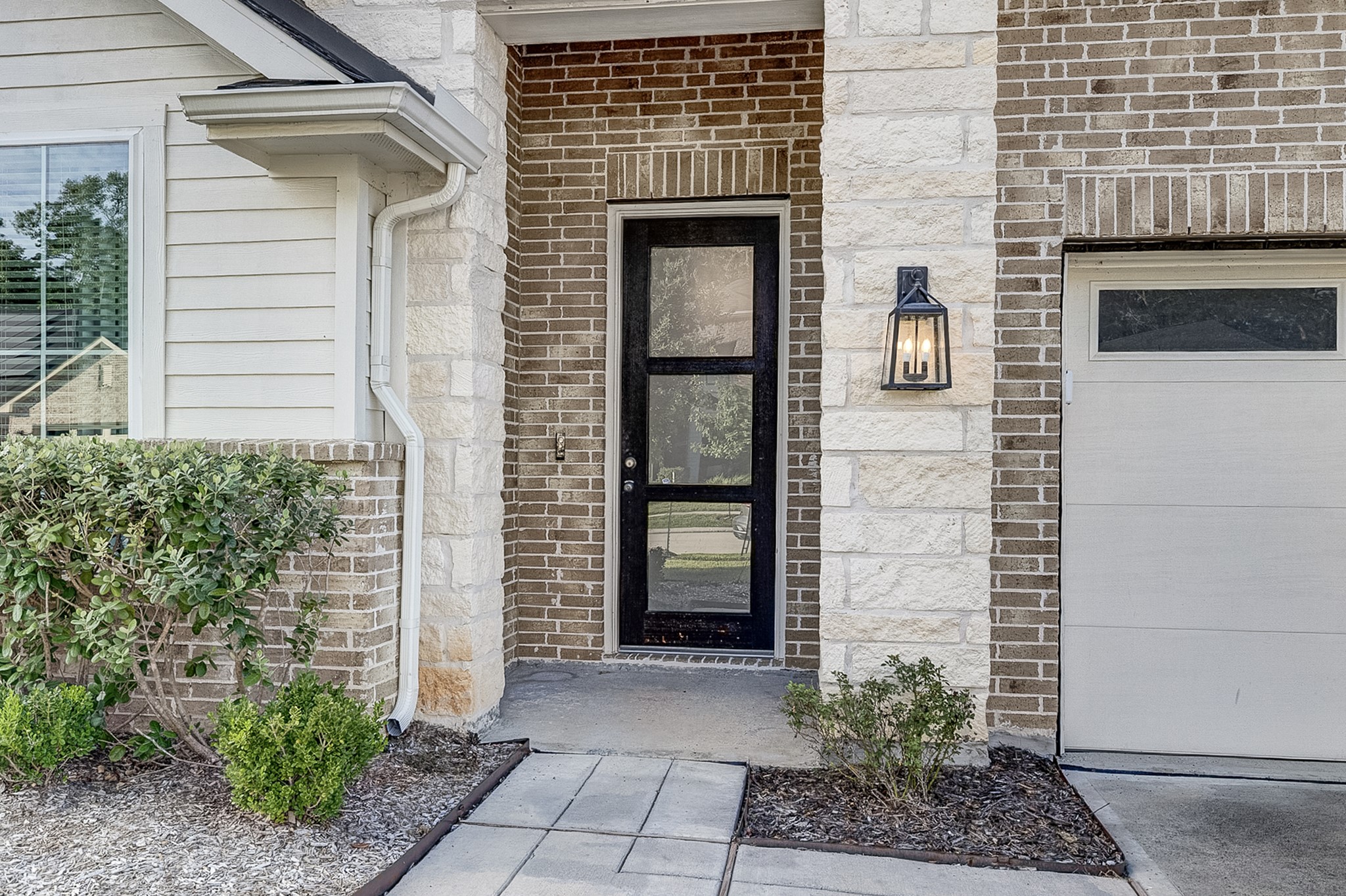 Charming front entrance featuring a modern glass door, elegant brick and stone accents, and a stylish outdoor light fixture.