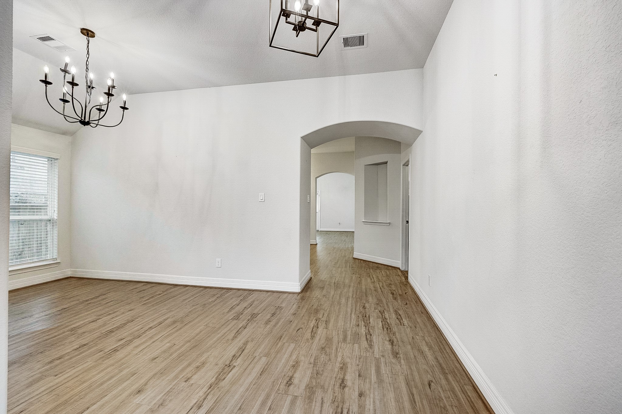 Spacious room with elegant chandeliers, wood flooring, and arched entryways, offering a bright and inviting atmosphere.