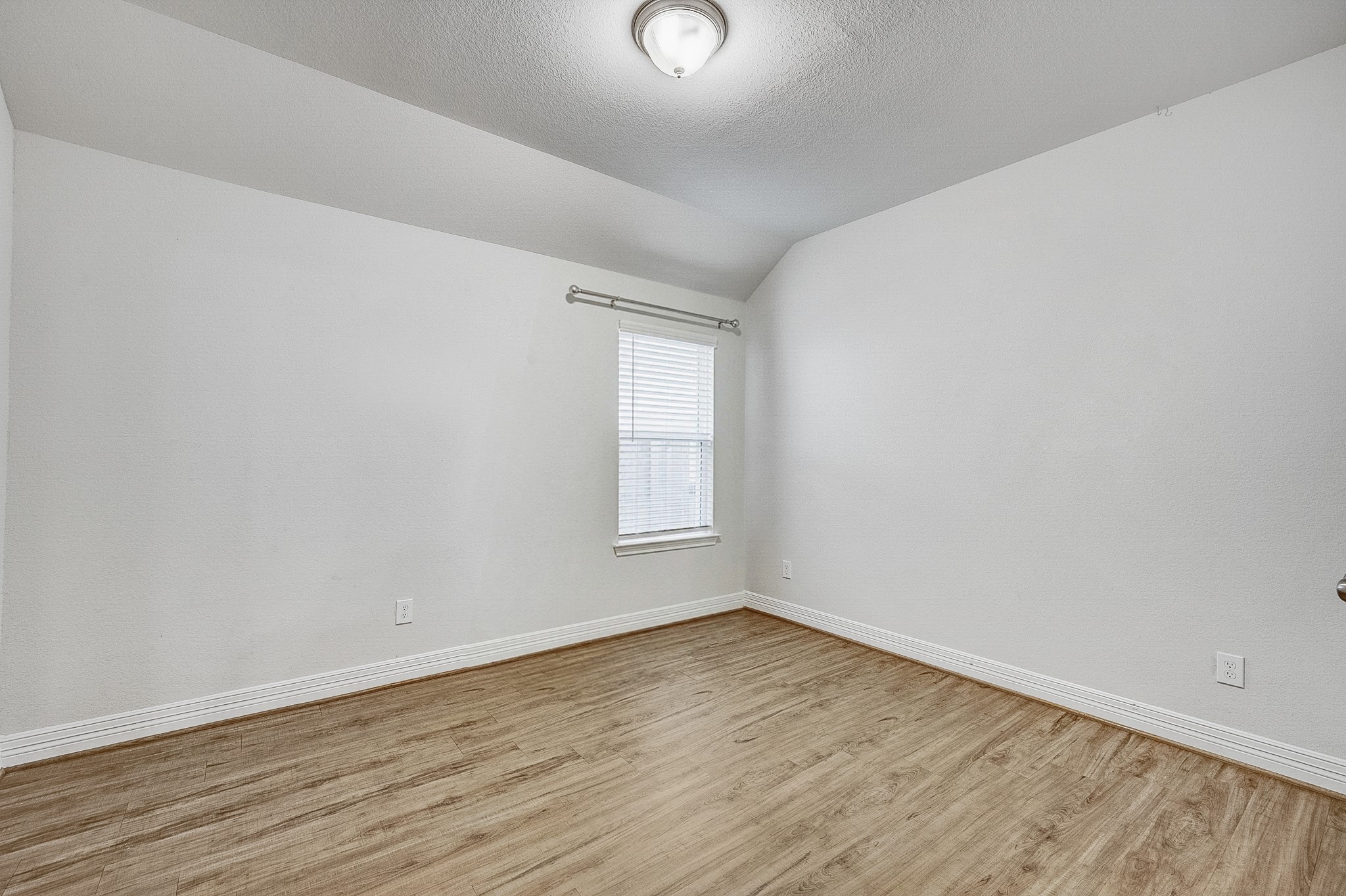 Bright and inviting room featuring sleek wood flooring, neutral walls, and a large window that fills the space with natural light.