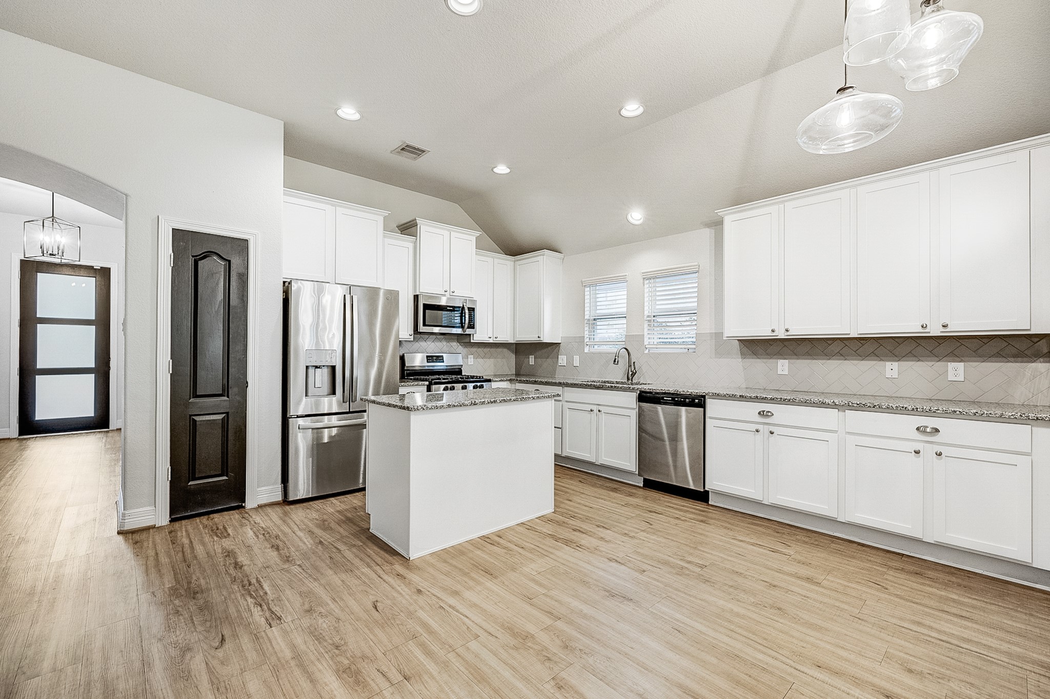 Spacious kitchen featuring sleek stainless steel appliances, pristine white cabinetry, and elegant granite countertops, complemented by warm wood flooring and modern lighting.