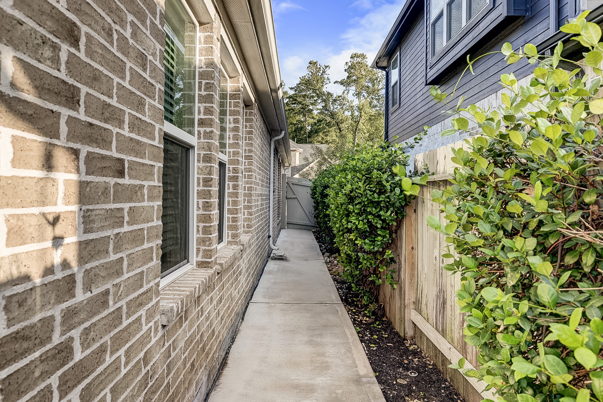 Charming side pathway with brick exterior and lush greenery, leading to a private backyard.