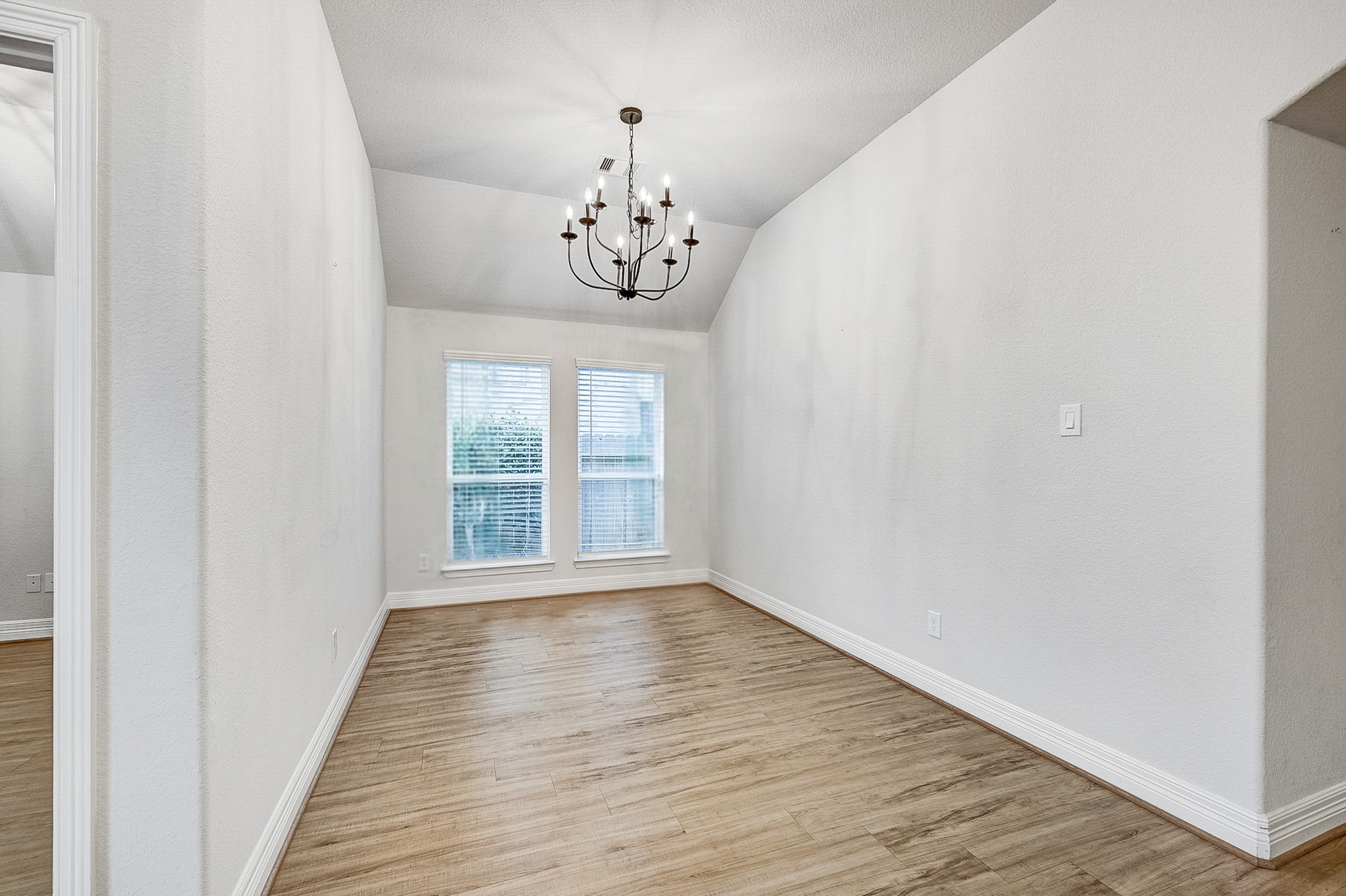 Elegant dining room featuring a stylish chandelier, vaulted ceiling, and abundant natural light through large windows, complemented by beautiful wood flooring.