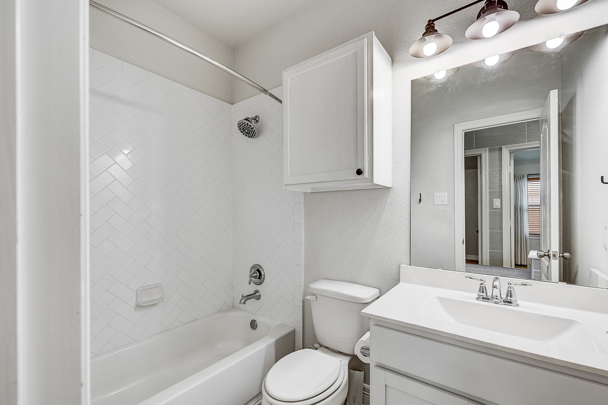 Bright and modern bathroom featuring a sleek vanity, spacious mirror, and a classic white-tiled shower-tub combo.