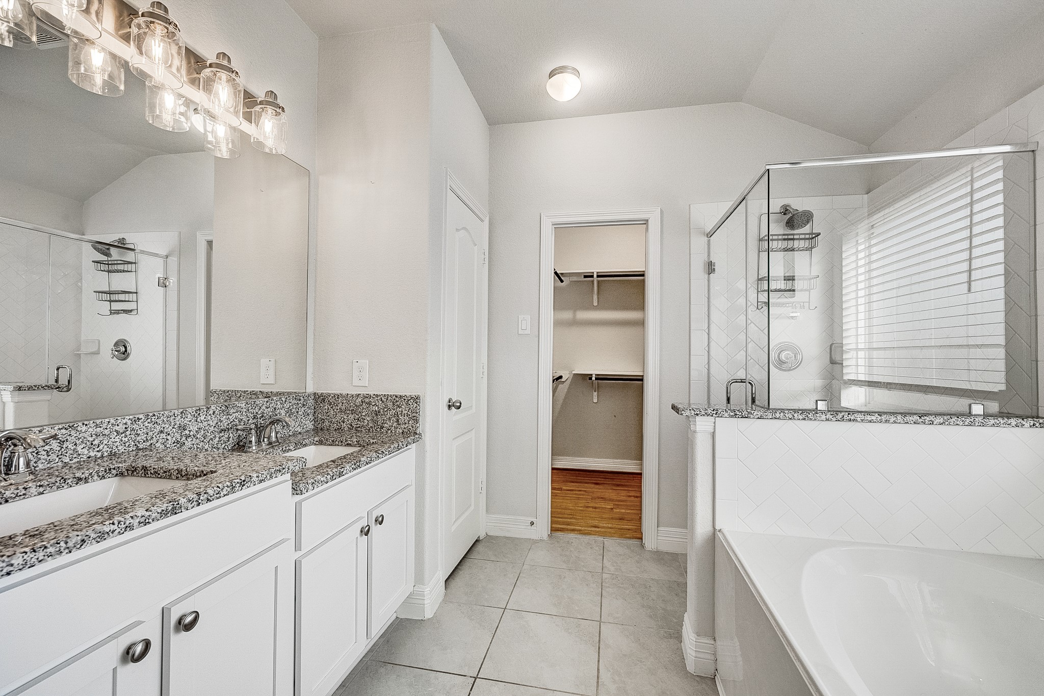 Elegant bathroom featuring a dual-sink vanity with granite countertops, a spacious glass-enclosed shower, and direct access to a walk-in closet.