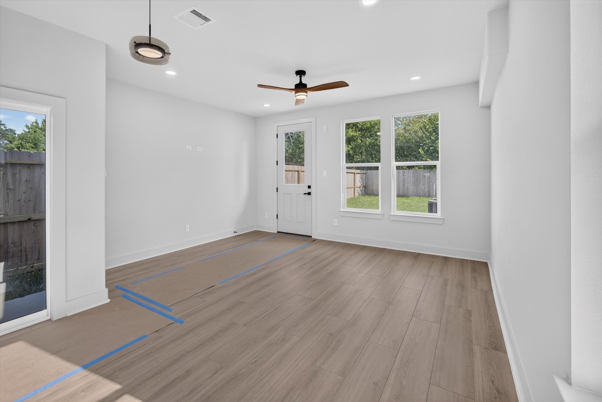 This open-concept kitchen and living area features a sleek island with a marble countertop, modern pendant lighting, and light wood cabinetry. The space is bright and airy with large windows, stylish gray walls, and wood-look flooring, providing a contemporary and inviting atmosphere.