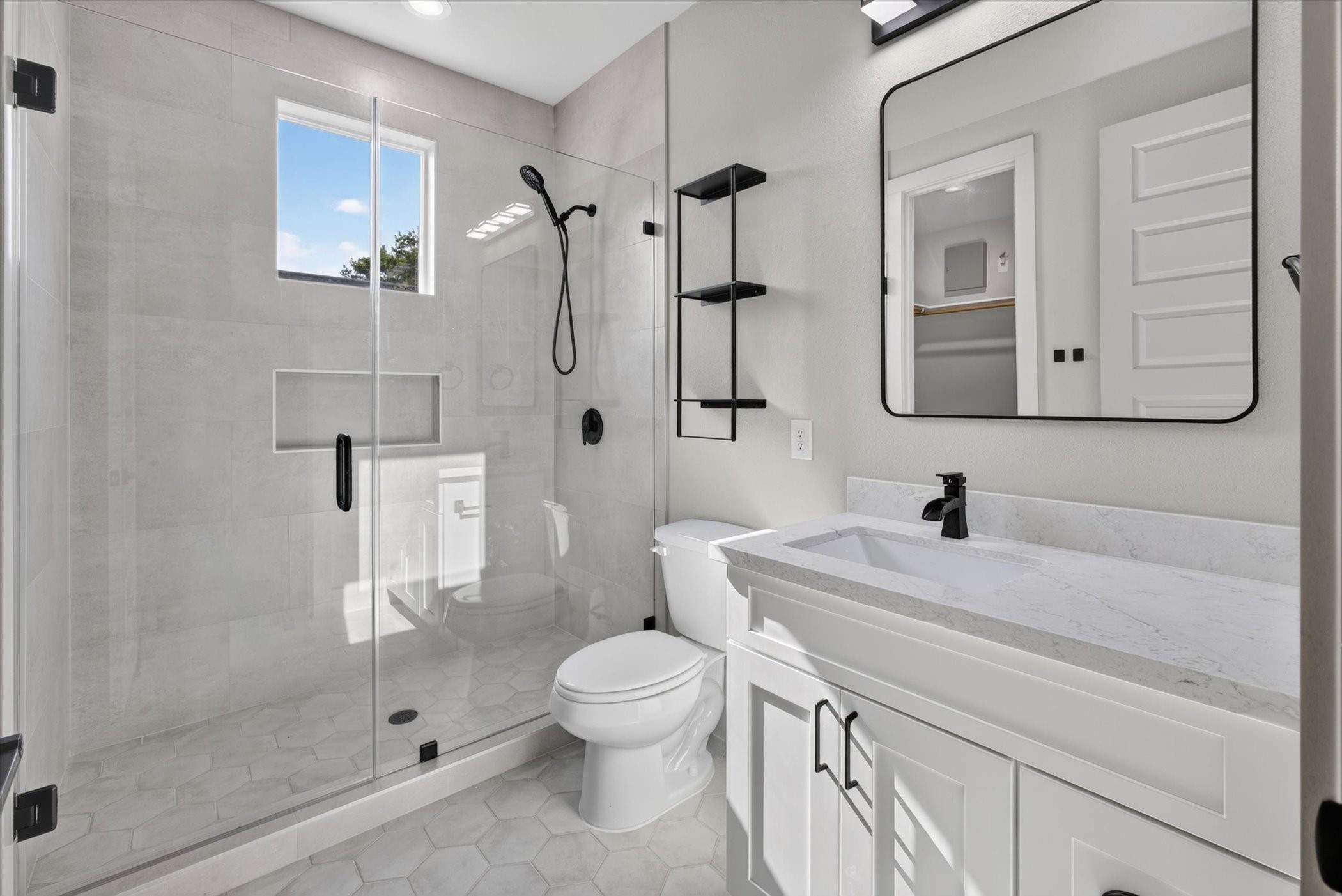 This modern bathroom features a sleek glass-enclosed shower with green tile, a stylish vanity with ample storage, and a neutral color palette. The space is enhanced by elegant fixtures and tasteful decor, creating a clean and inviting atmosphere.