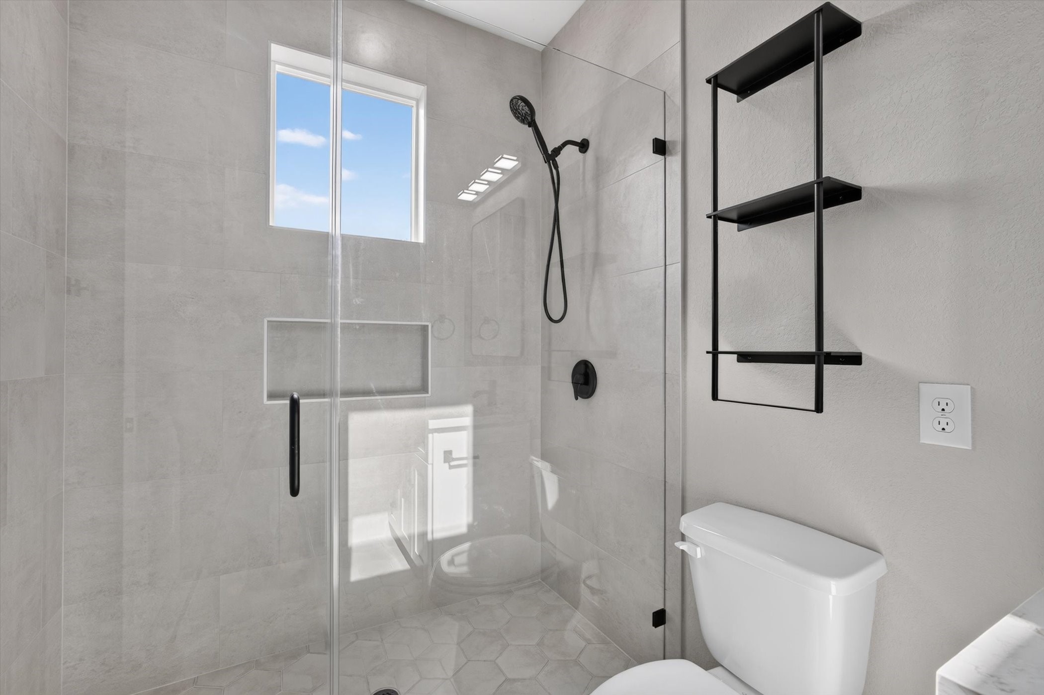 This modern bathroom features a sleek wooden vanity with a white countertop and a rectangular mirror. A neutral gray wall complements the clean design, and a touch of greenery adds a fresh accent.