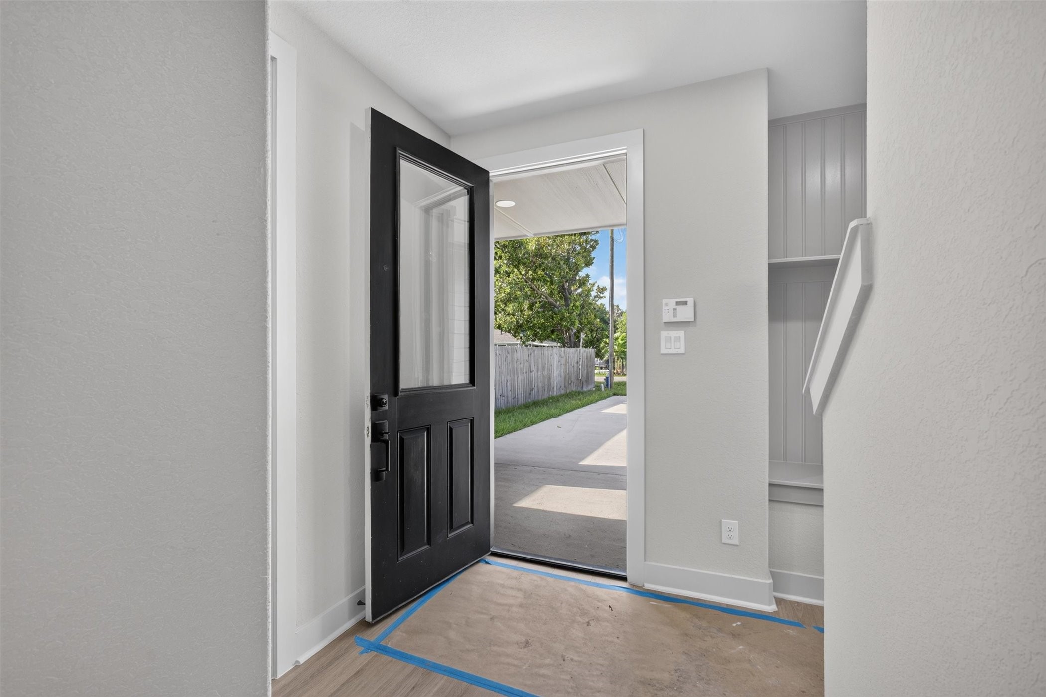 This entryway features a modern design with a large windowed door, stylish dark walls, and wood flooring. There is a cozy nook with seating and shelving, plus a small window for natural light. A staircase leads upward, adding to the home's welcoming ambiance.