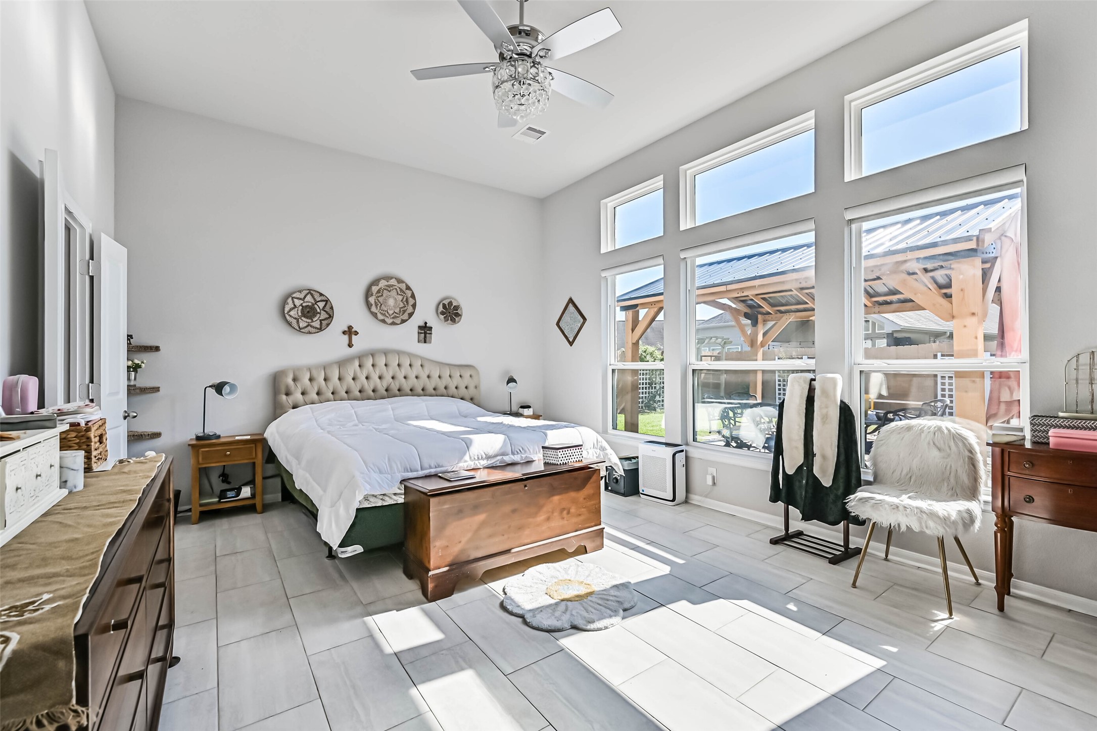 Spacious primary bedroom featuring high ceilings, abundant natural light, a wall of windows, and a ceiling fan with decorative lighting.