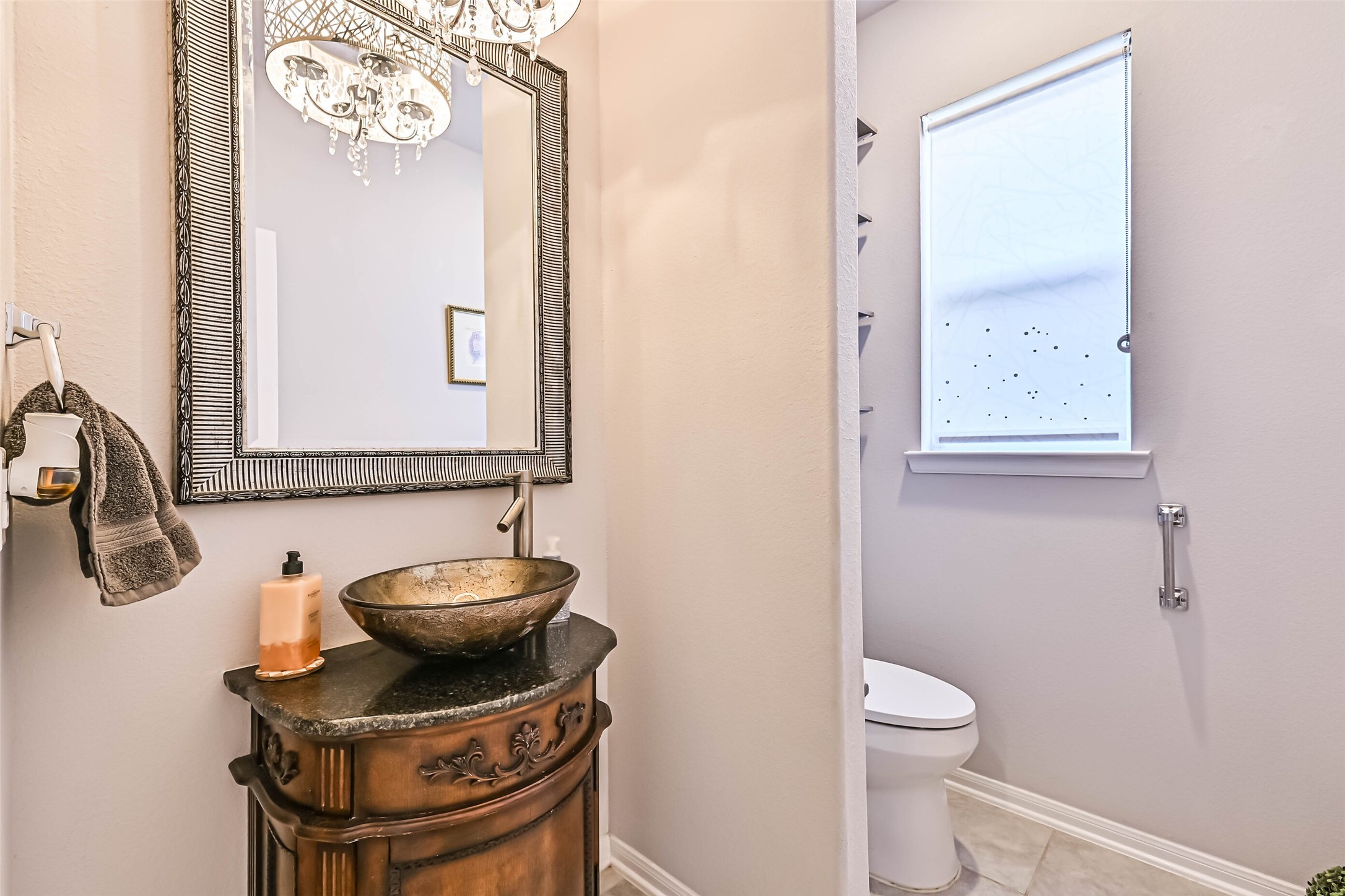 Charming half bath featuring a decorative vessel sink, custom-style vanity, framed mirror, and elegant light fixture.