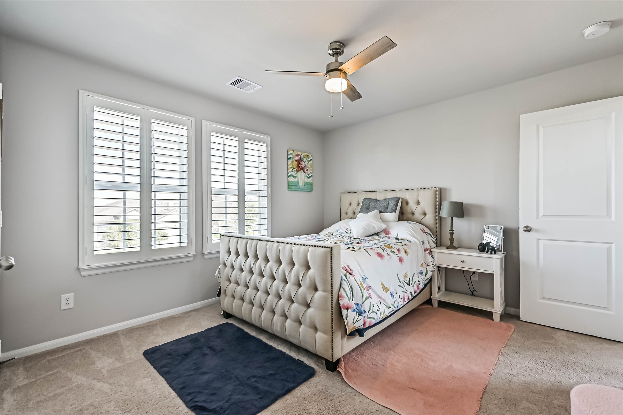 Another view of the bedroom showcasing its generous layout, plantation shutters, and neutral finishes.