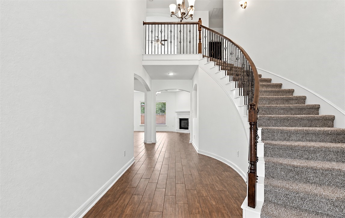 Step inside to a grand two-story entryway with a sweeping curved staircase, wrought iron railing, hardwood floors, and a chandelier that makes every entrance feel special.