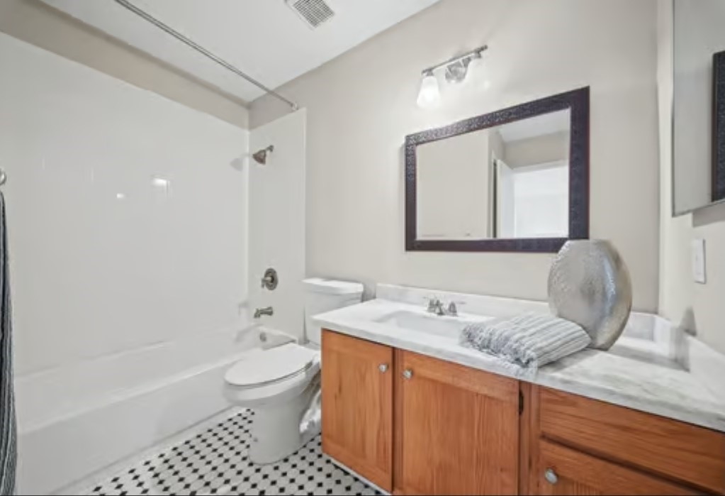 Charming 2nd bathroom featuring a classic black-and-white tile floor, a spacious vanity with wood cabinetry, and a modern mirror. The shower-tub combo adds functionality and style. An addition half bathroom is located downstairs in the hallway