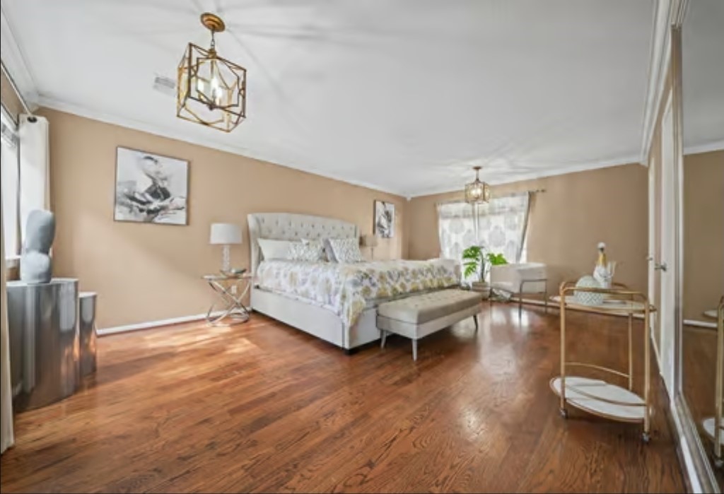 Spacious primary owners suite bedroom has rich hardwood floors, has large closet space, and ample natural light from large windows.